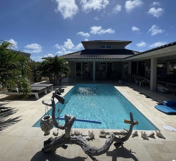 Modern indoor space with large glass doors, lush greenery, and a cozy seating area visible beyond.