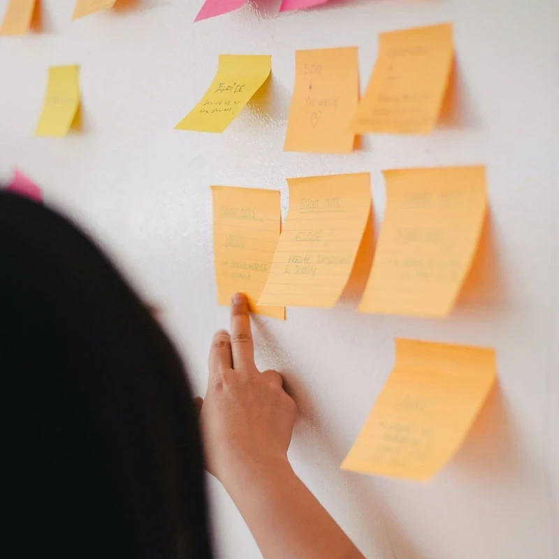photo of a person pointing to a group of postits on a whiteboard