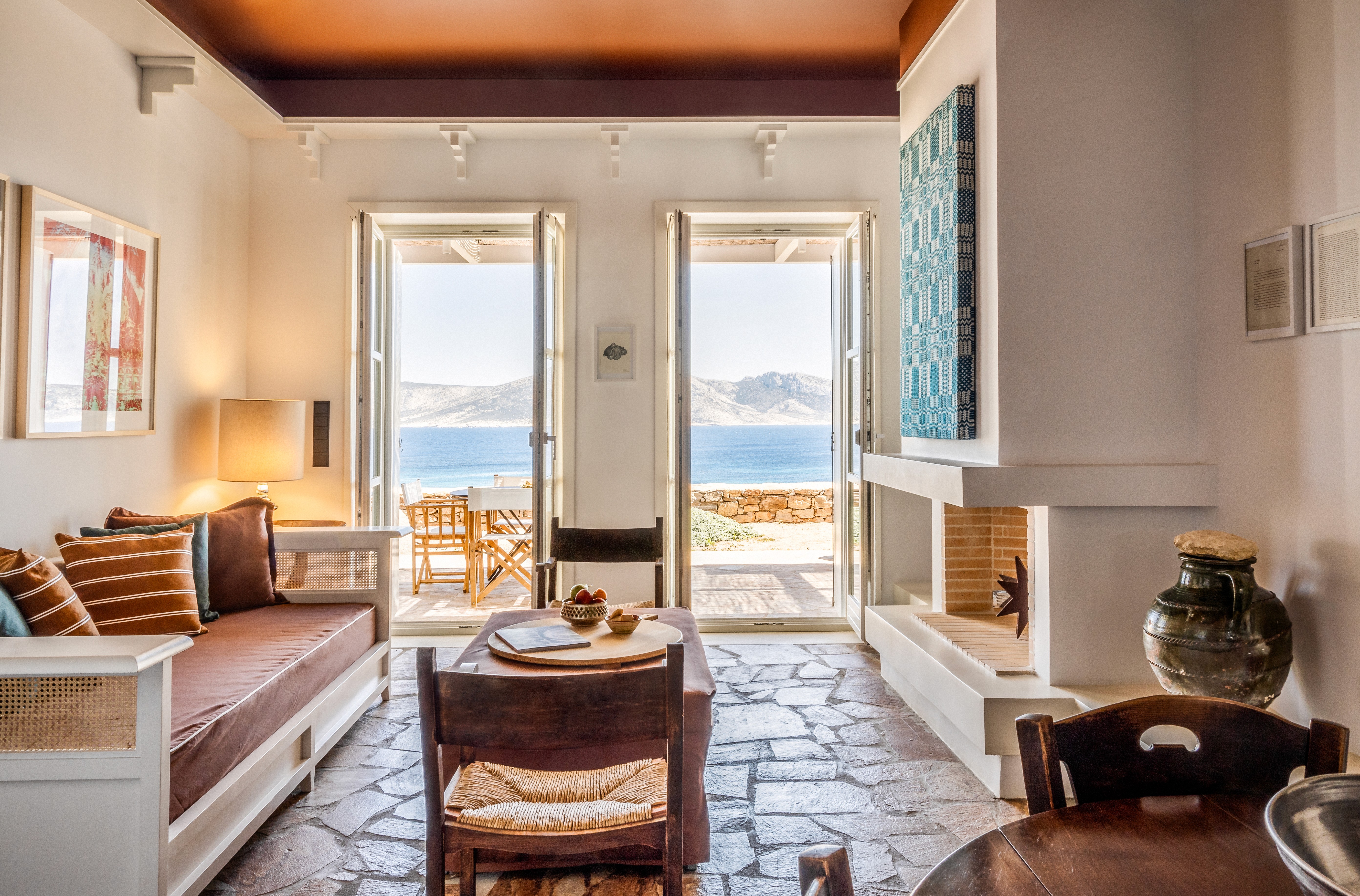 Living room with a sofa, a coffee table and art on the wall with open windows looking onto the mediterranean sea