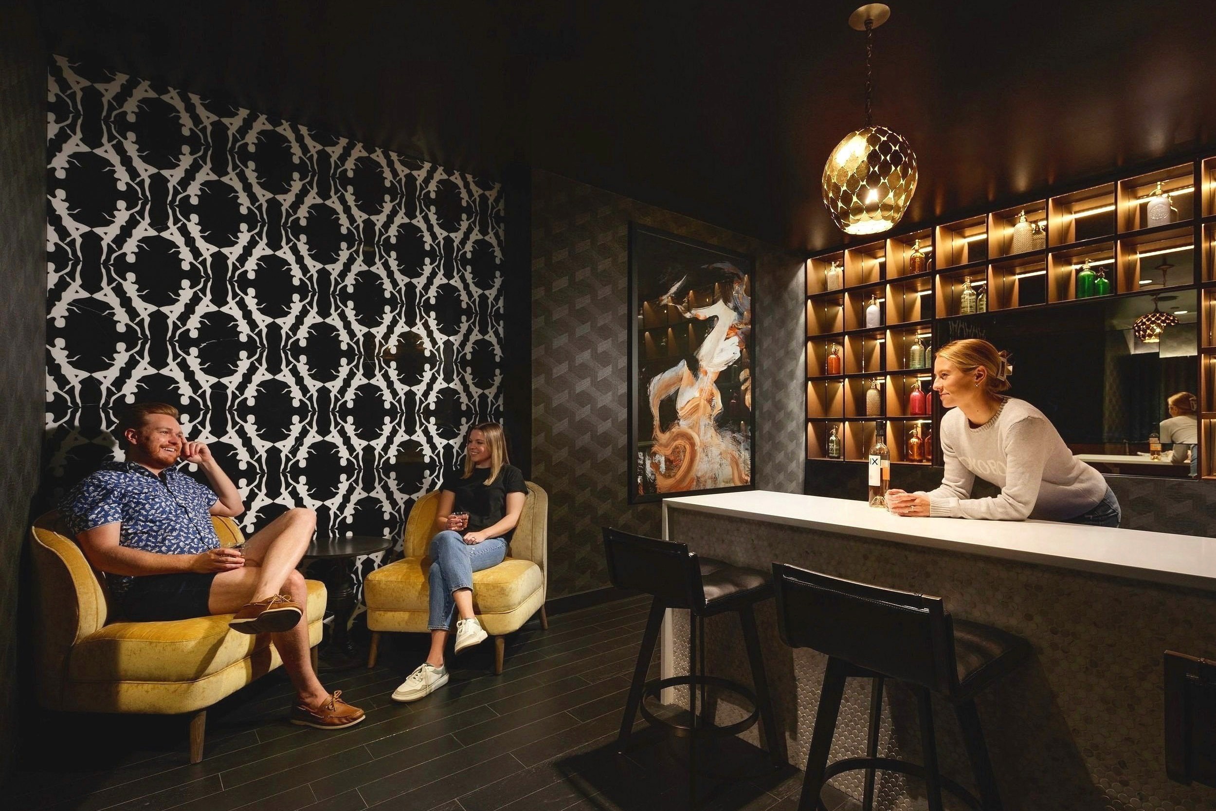 People in modern lounge with bar and patterned wallpaper.