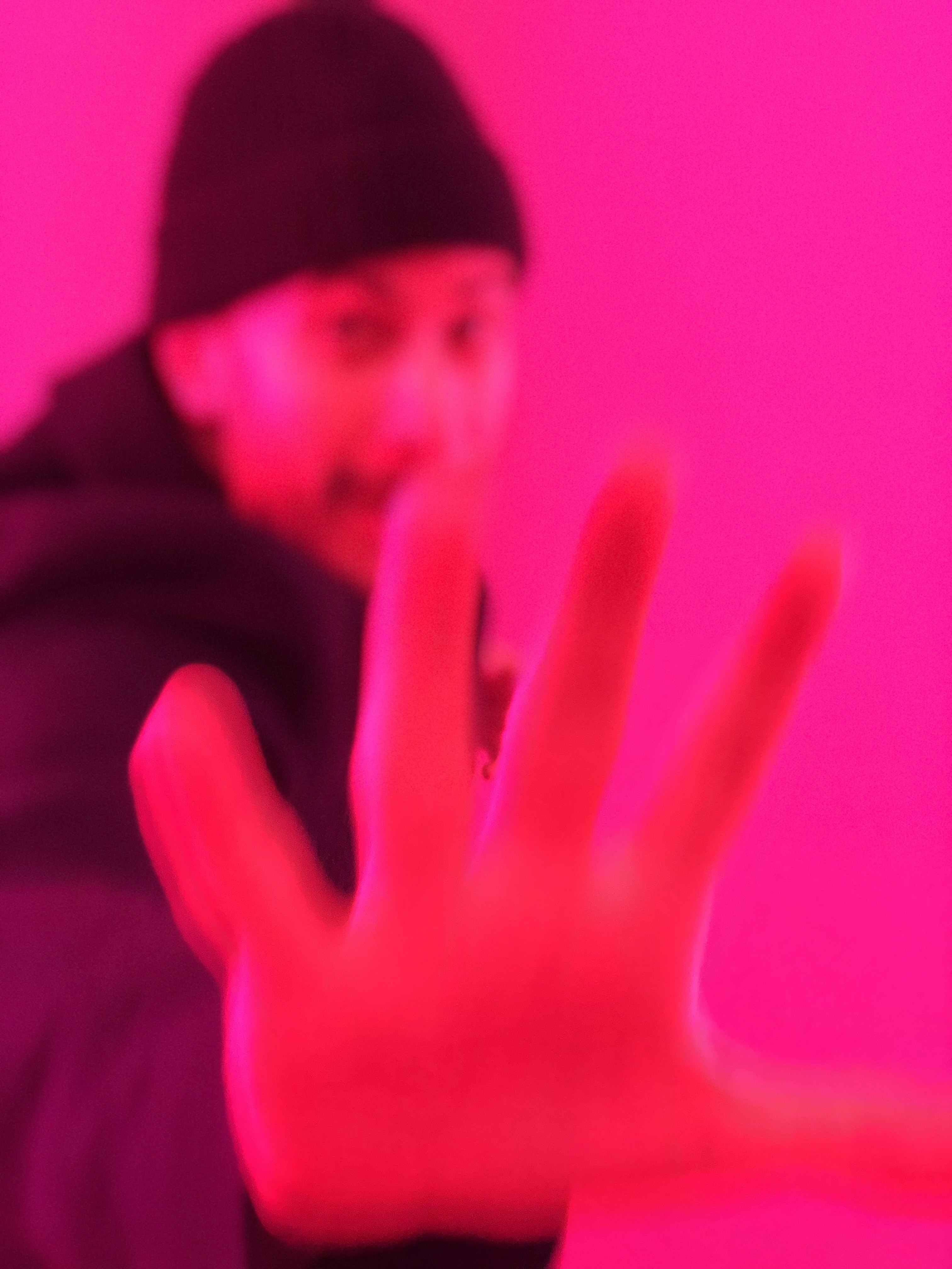 Person wearing a blue puffer jacket and red backpack standing in front of a light blue building on a city street.