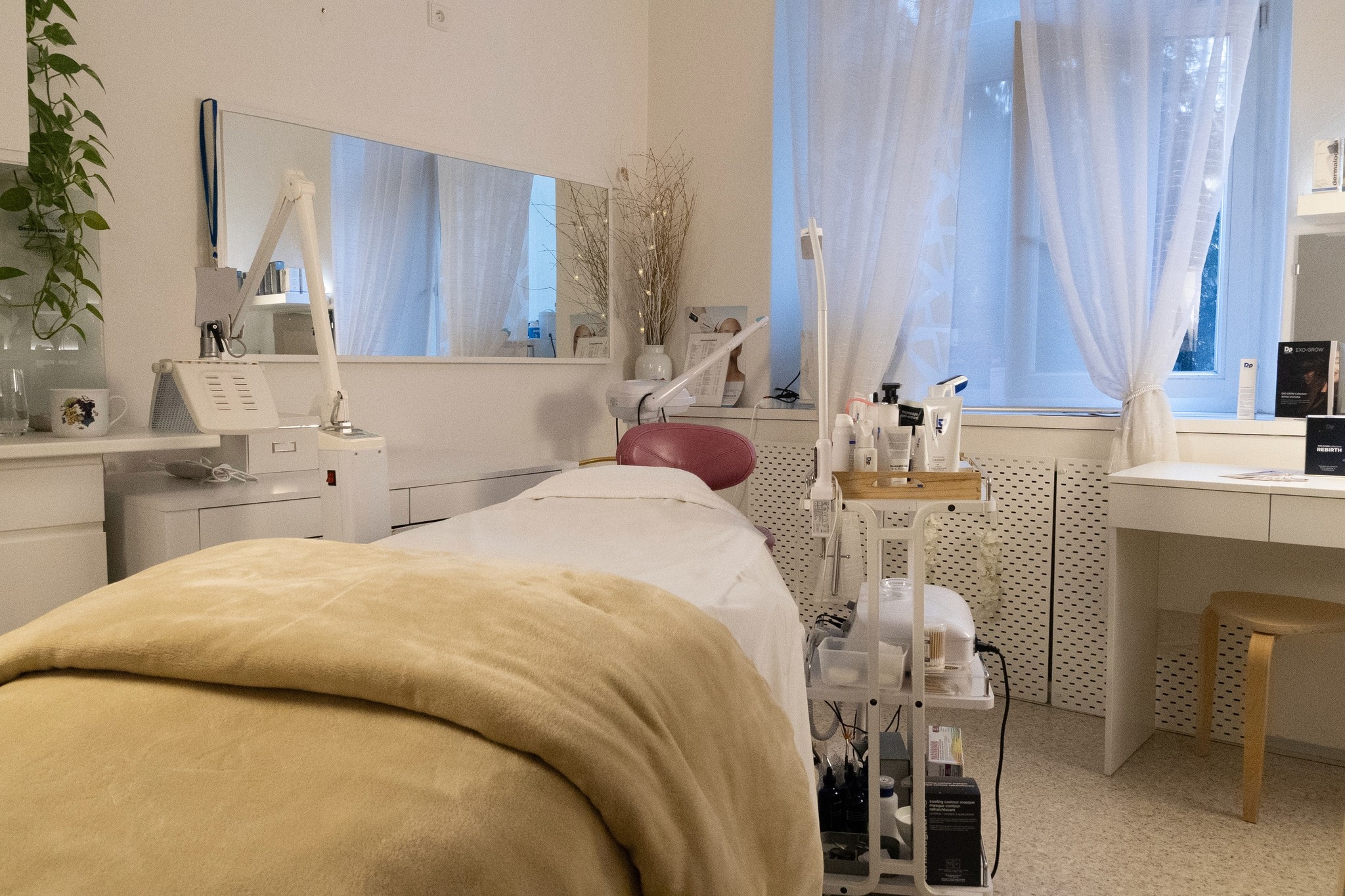 Kosmetické studio s ošetřovacím lehátkem, béžovou dekou, přístroji na pleťové ošetření a velkým zrcadlem