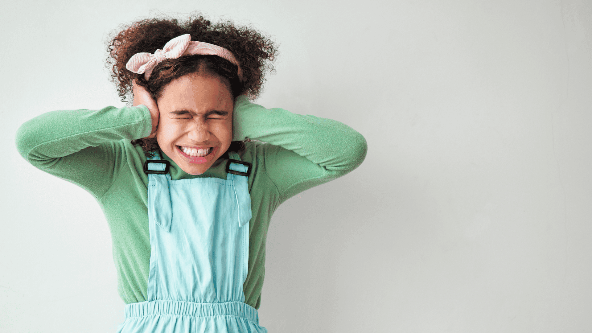 A young girl standing and covering her ears, looking stressed during a meltdown.