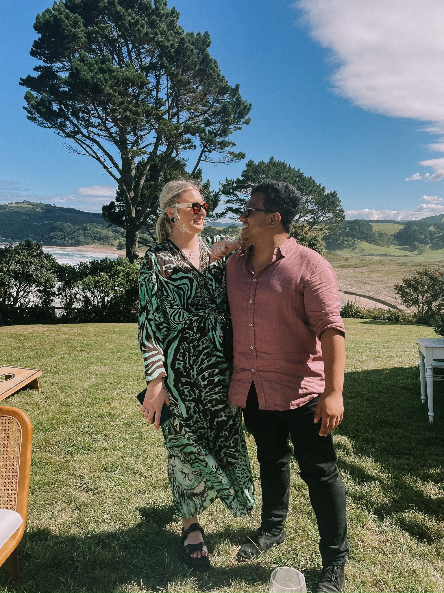 A bride and groom hold hands tenderly, the bride's bouquet of dried flowers hanging low. They stand in a softly lit, elegant interior, conveying romance.