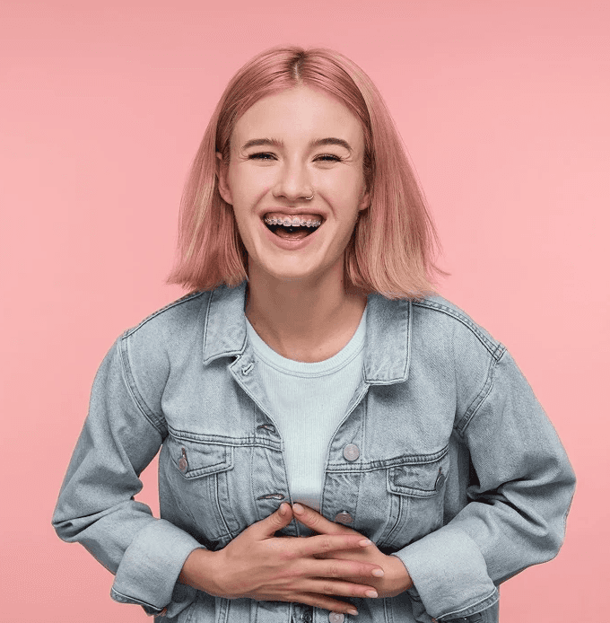 Junge Frau mit rosa Haaren lacht – modernes Lächeln nach kieferorthopädischer Behandlung.