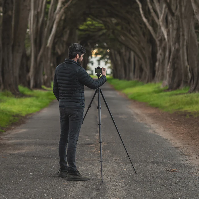Man touching camera on tripod on a forest road