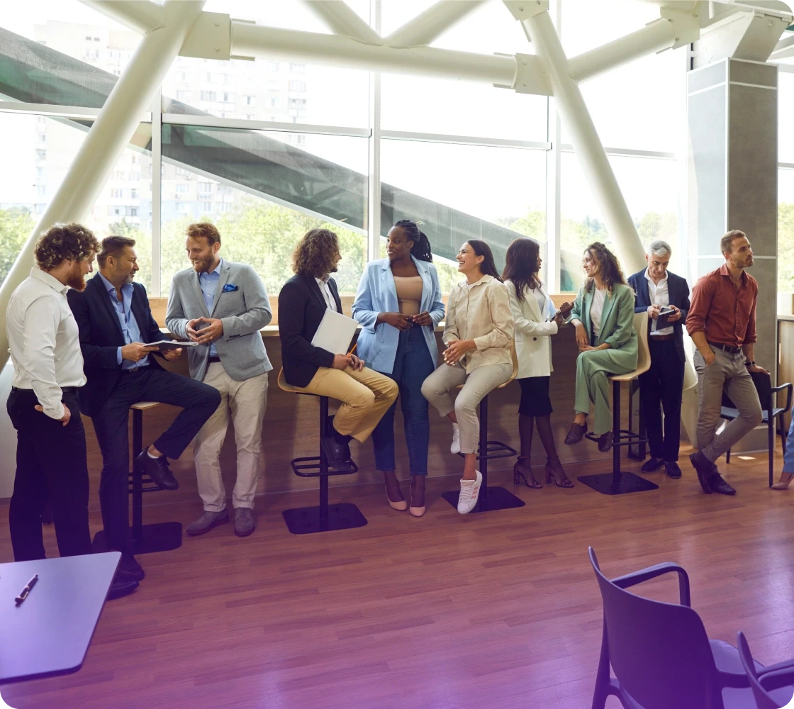 Group of people standing and chatting inside a modern space with large windows and natural light.