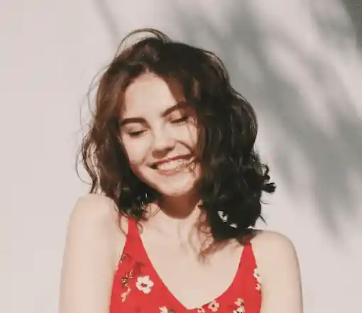 Jeune femme brune dehors devant un mur blanc