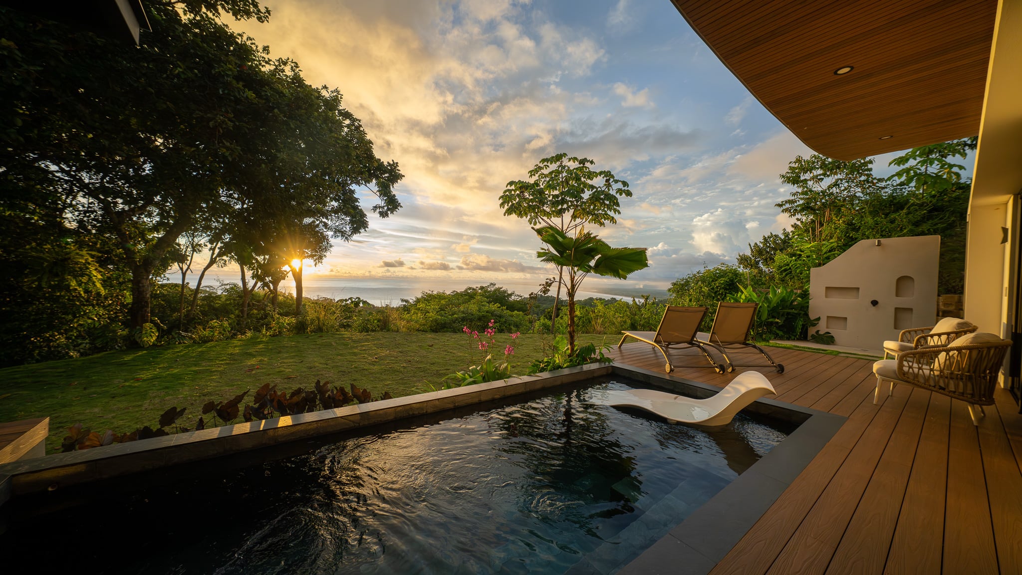 Private plunge pool with sun loungers and a white outdoor shower on a wooden deck surrounded by tropical landscaping.