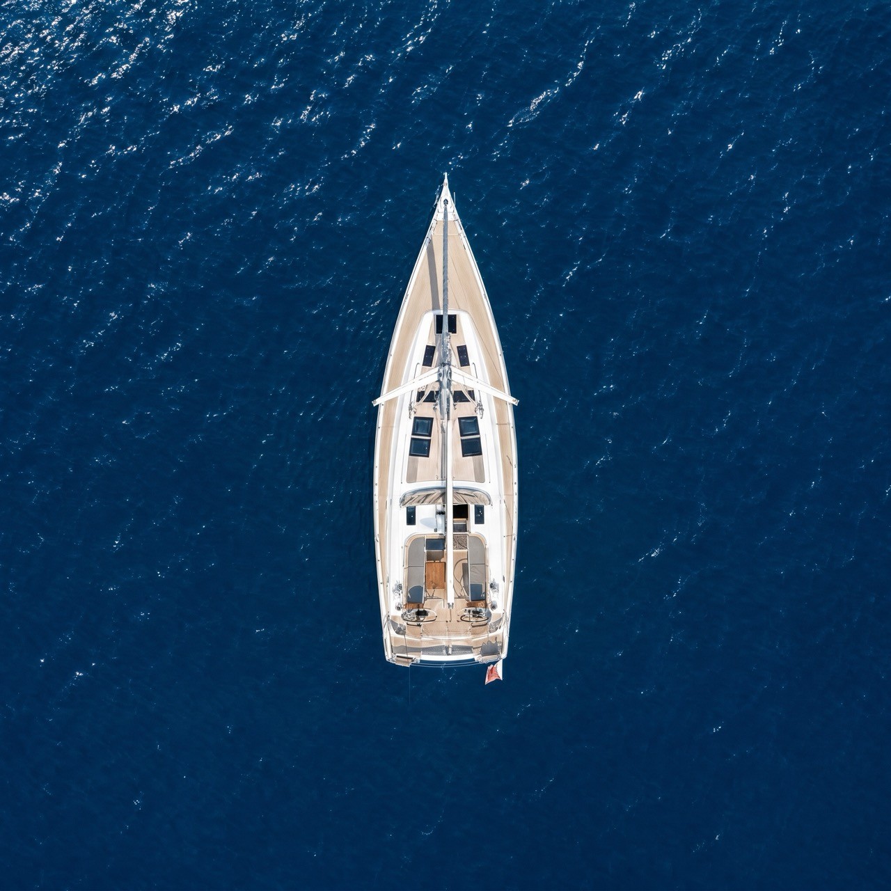 Overhead night aerial photograph of a Beneteau Clipper 361 sailing yacht with warm interior cabin lighting illuminating the teak deck, set against a dark black ocean background