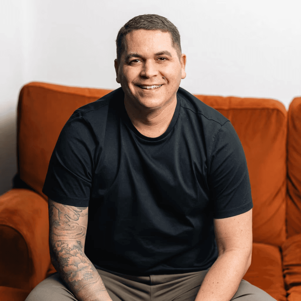 Man in black t-shirt and khaki pants on orange couch.