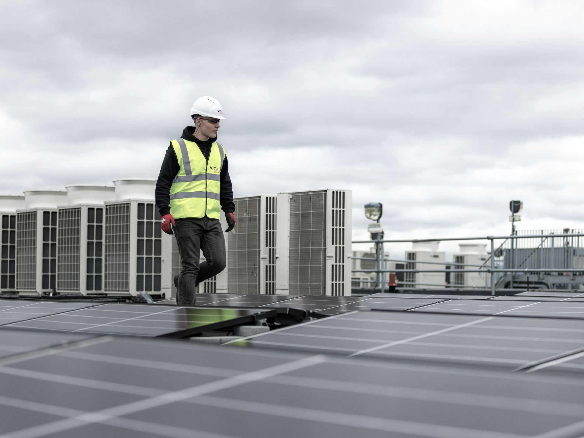 Technician in safety gear inspecting solar panel installations on a commercial rooftop