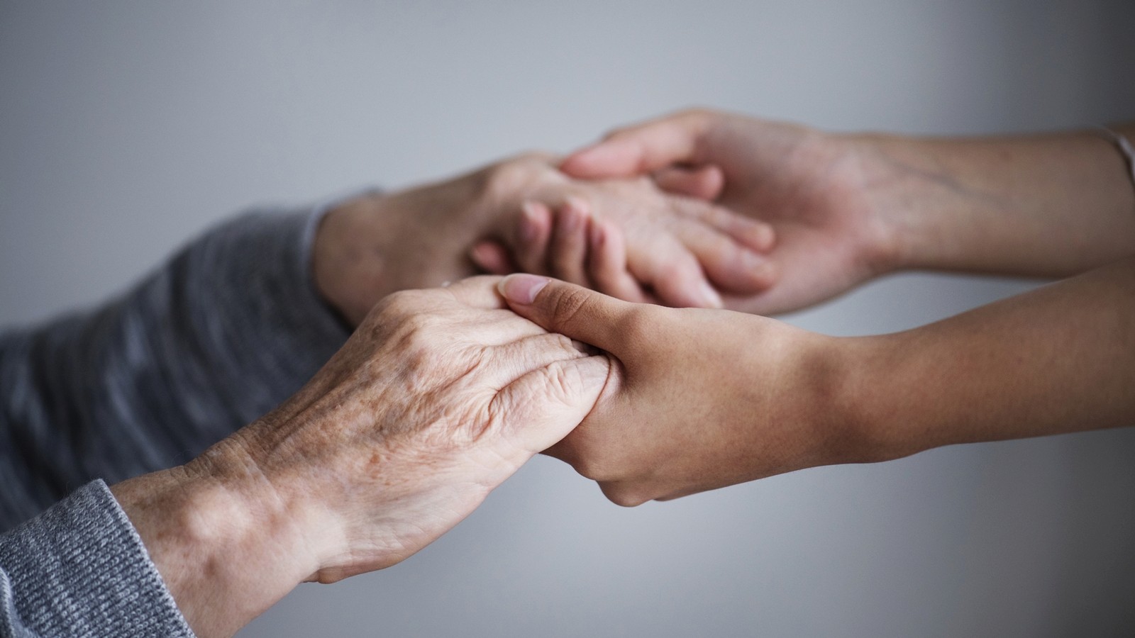 Mulher segurando mãos de pessoa idosa
