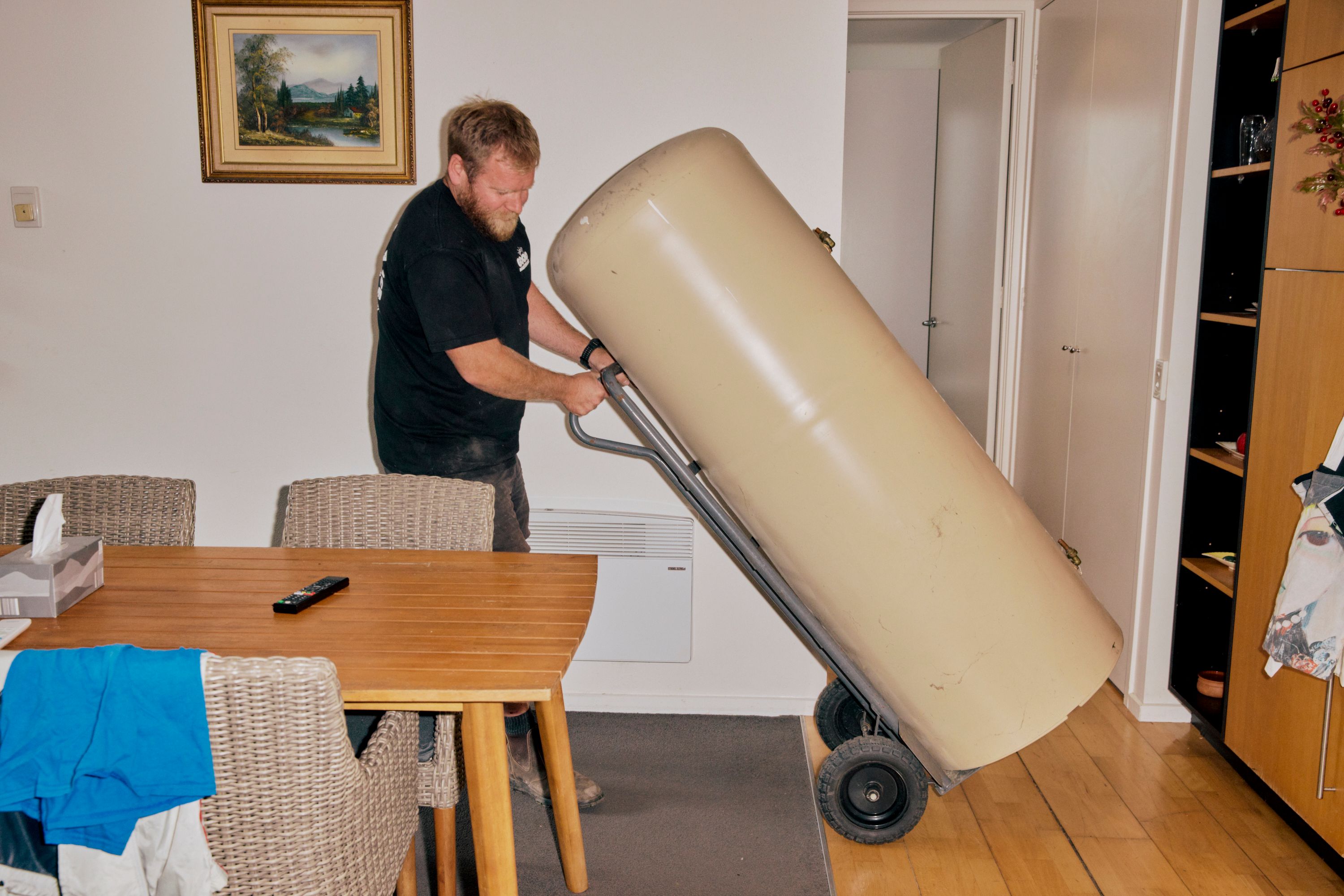 A Good Maintenance Technician wheeling a hot water system on a trolly inside a rental property.