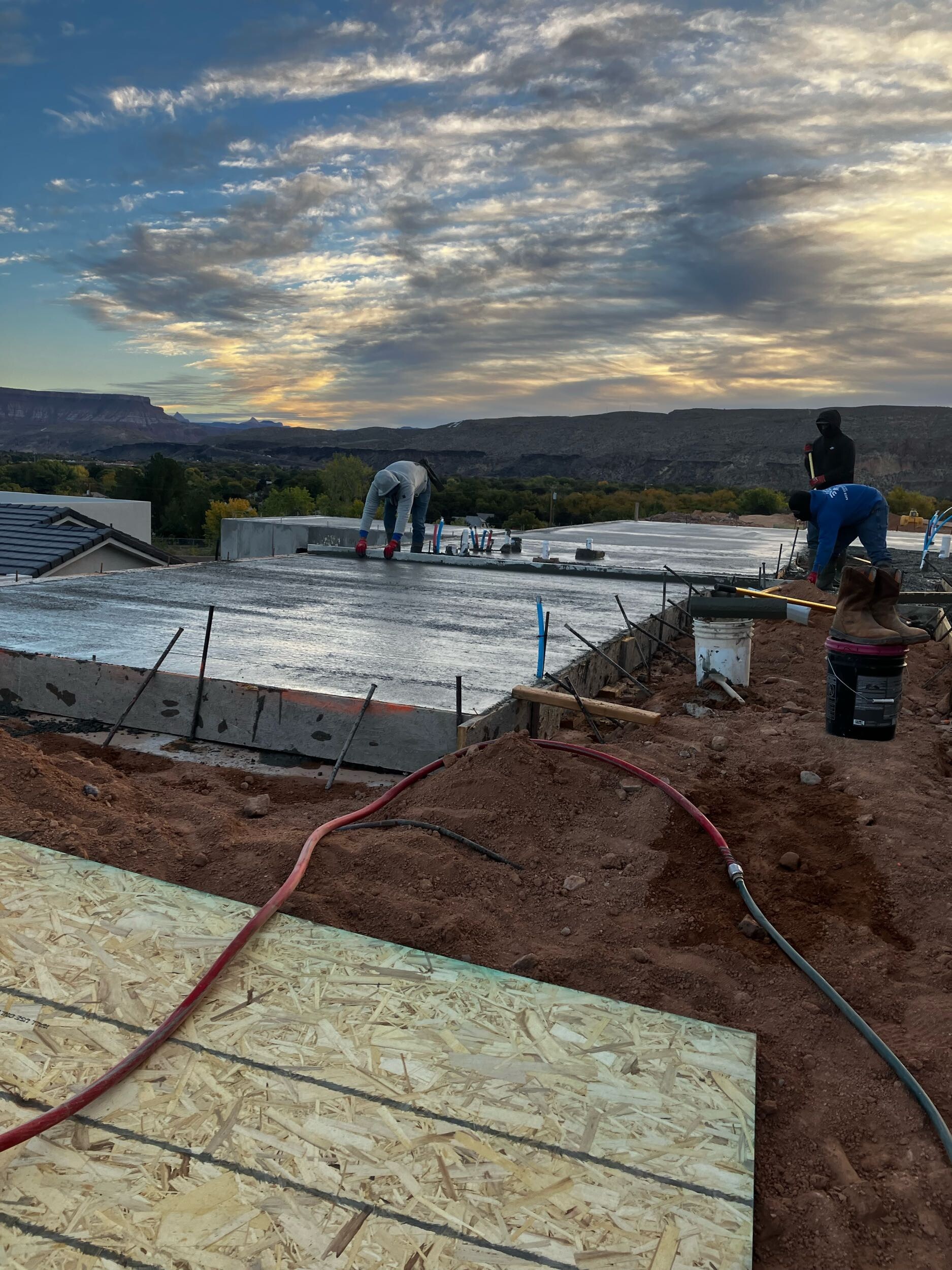 Concrete foundation pour for a custom home in Hurricane, Utah, with red rock cliffs and mountains in the background at sunrise.