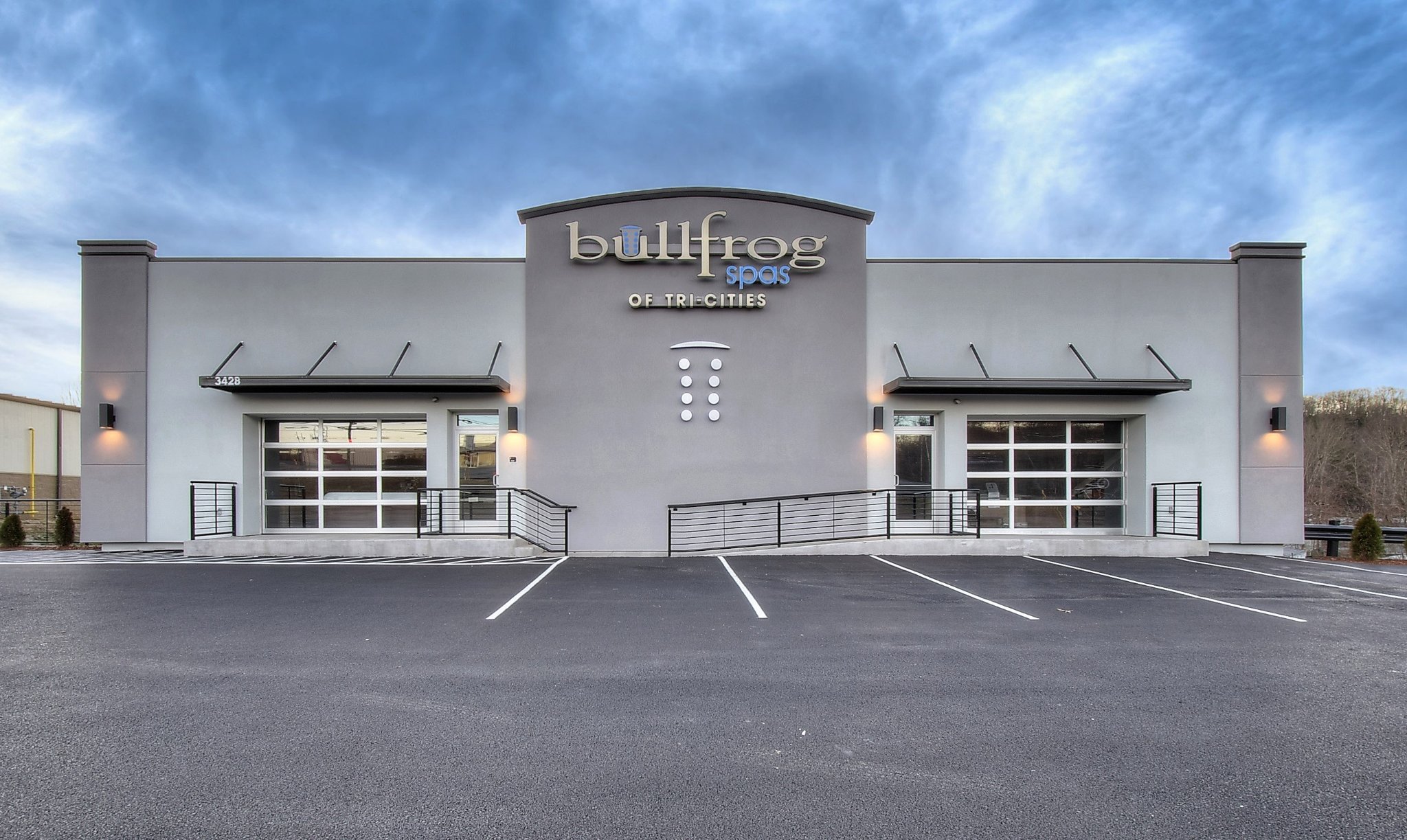 A modern commercial building with large windows and a gray facade, set against a cloudy sky.