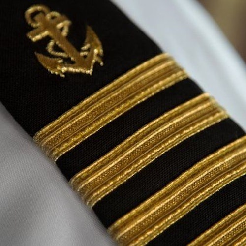 黑色制服肩章的特寫，帶有四條金條和繡著的錨和繩索徽章。