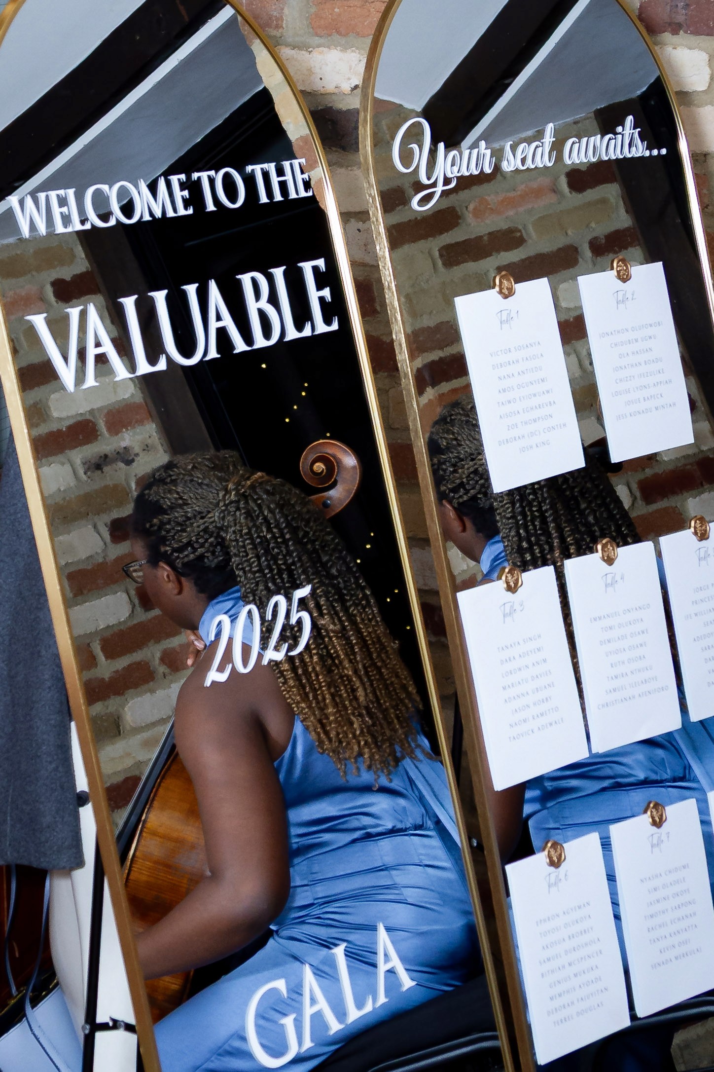 Welcome to the Valuable 2025 Gala sign with seating chart. Woman with braided hair in blue dress reflected.