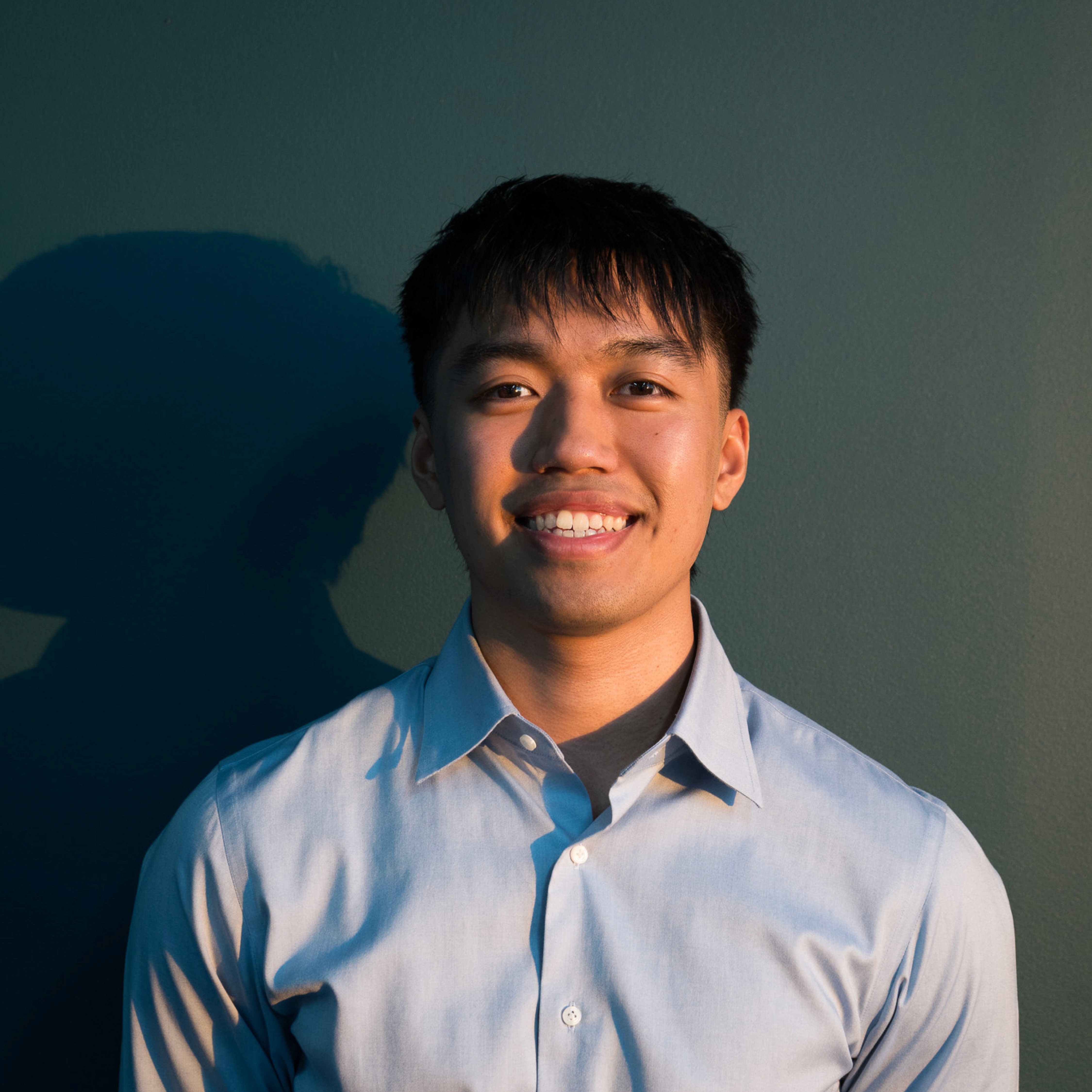 Portrait of Jhensen Mangalino, Managing Director at Conxept Agency, wearing a light blue shirt, smiling in front of a dark background with warm lighting.