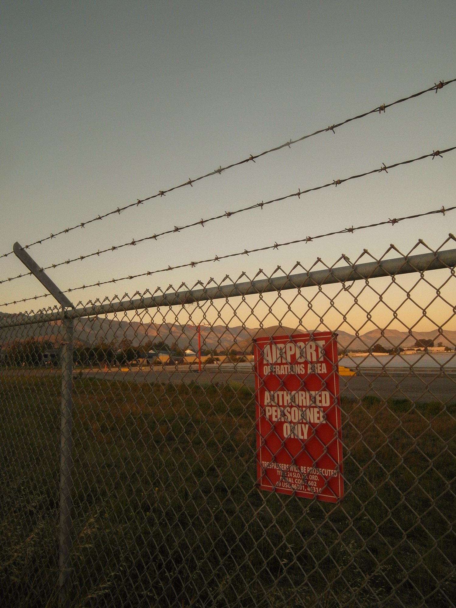 Chain-link fence and barbed wire with an authorized personnel only sign at golden hour.