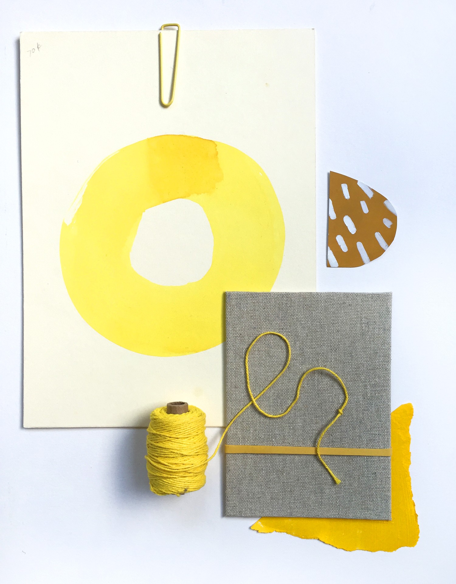 Assemblage of yellows and gold: oversized yellow circle, paper clip, yellow string, painted dark yellow shape, and blank tan bookcover with yellow rubber band