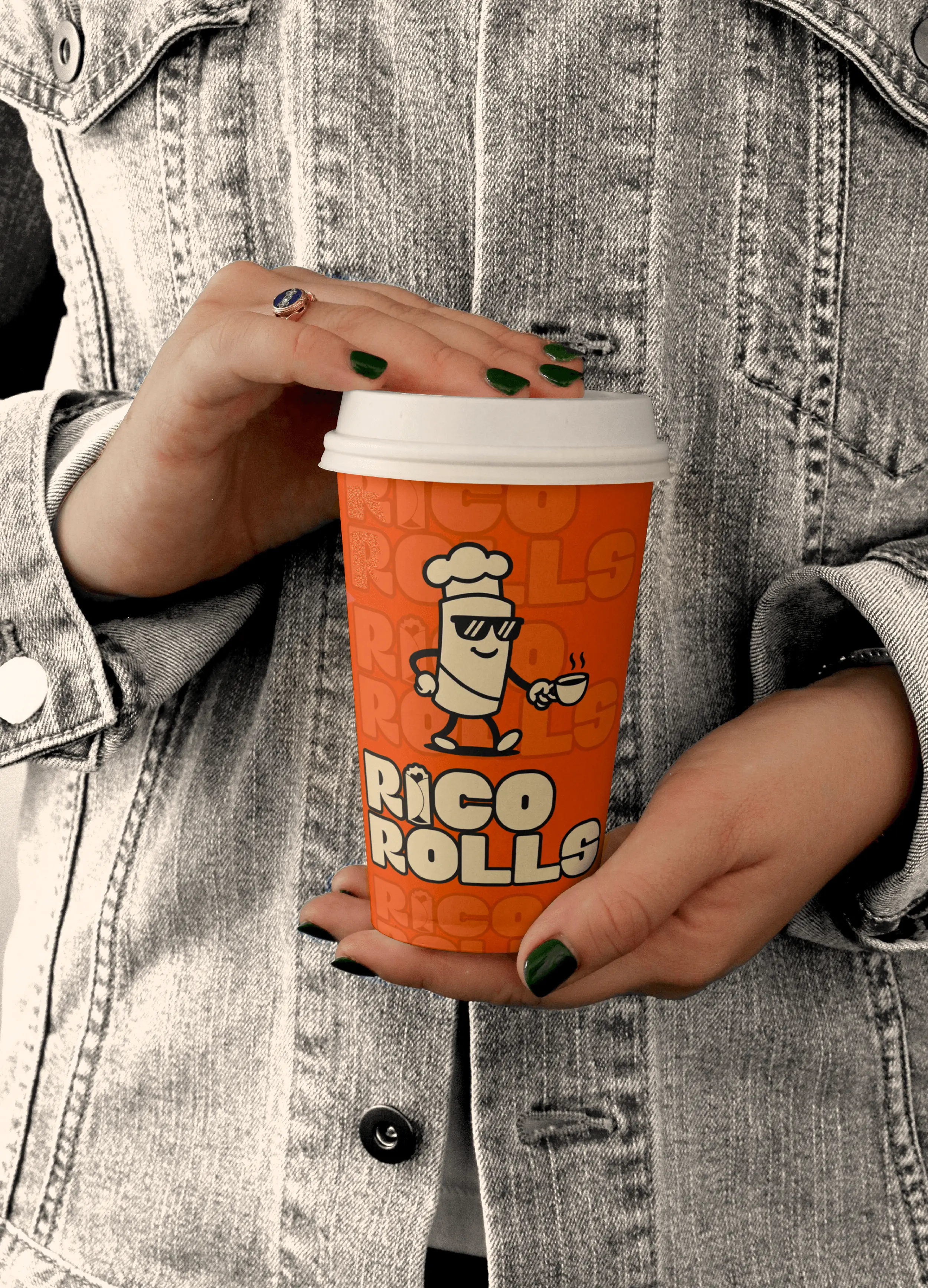 Person holding a Rico Rolls branded takeaway cup featuring the mascot illustration on a bright orange design, photographed against a denim jacket background.