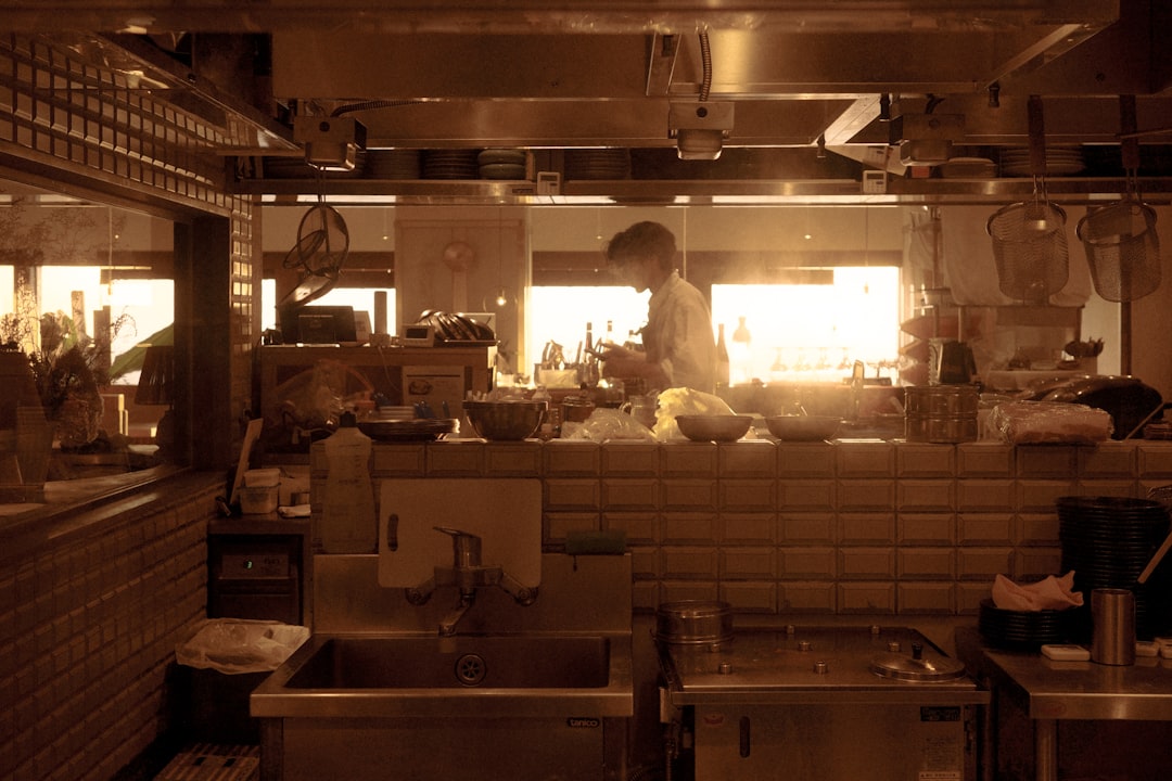 professional chef in white uniform using a high-precision digital scale to weigh portioned meat cuts in a commercial kitchen with stainless steel prep tables and copper pans hanging in the background, sharp focus, cinematic lighting
