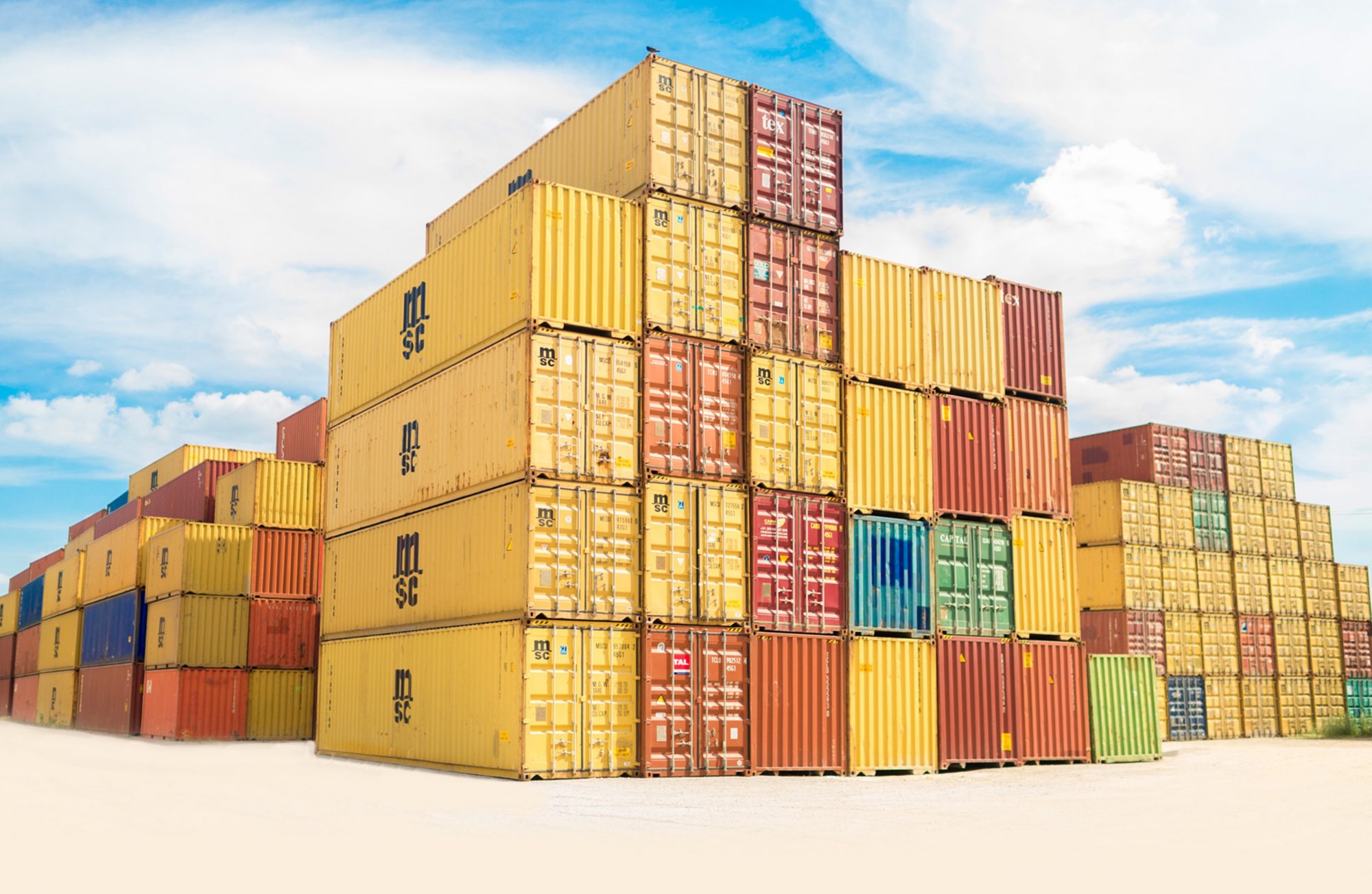A stack of colorful shipping containers against a blue sky with scattered clouds.