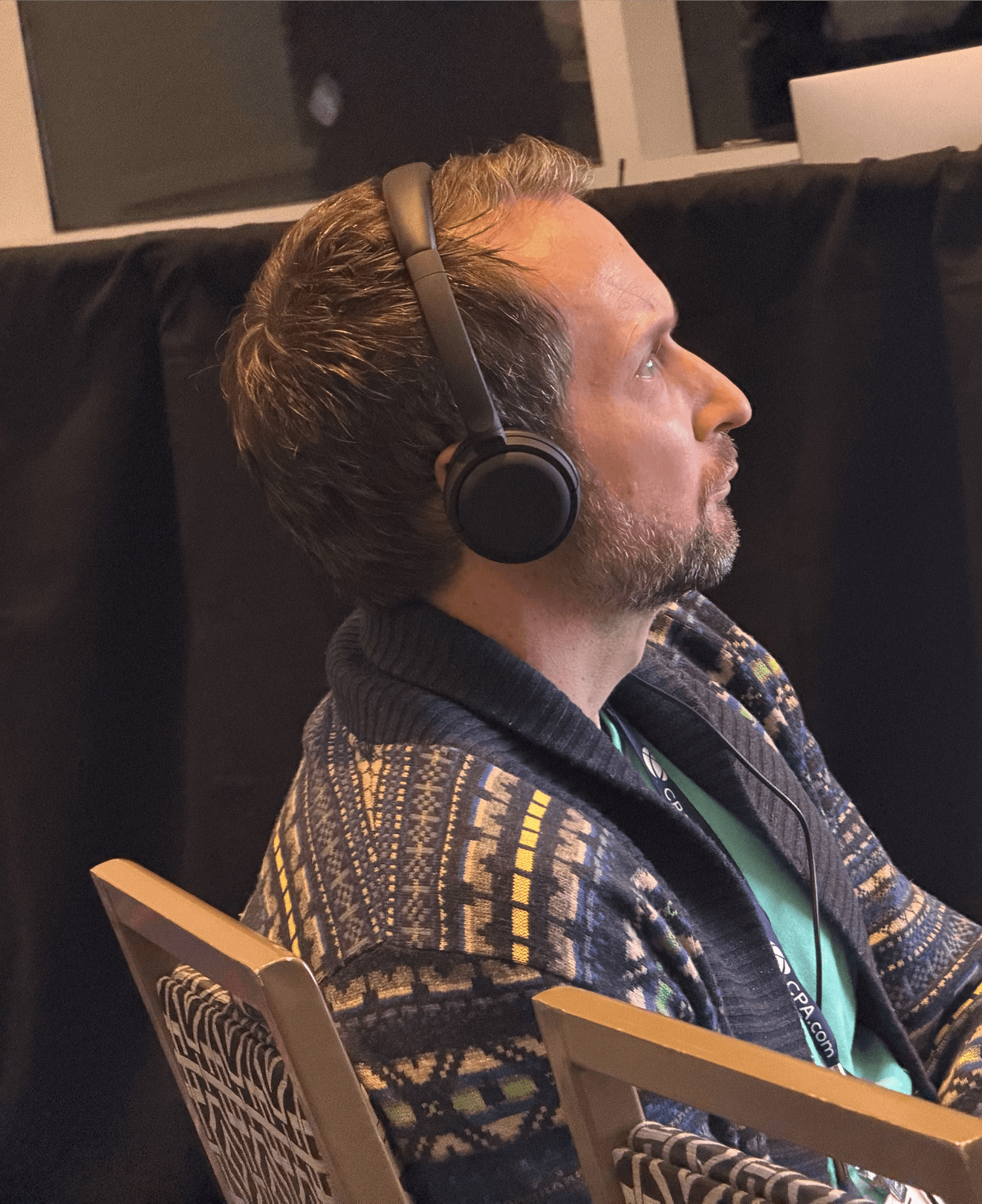 Man in a sweater smiling with arms crossed while standing by a wooden wall.