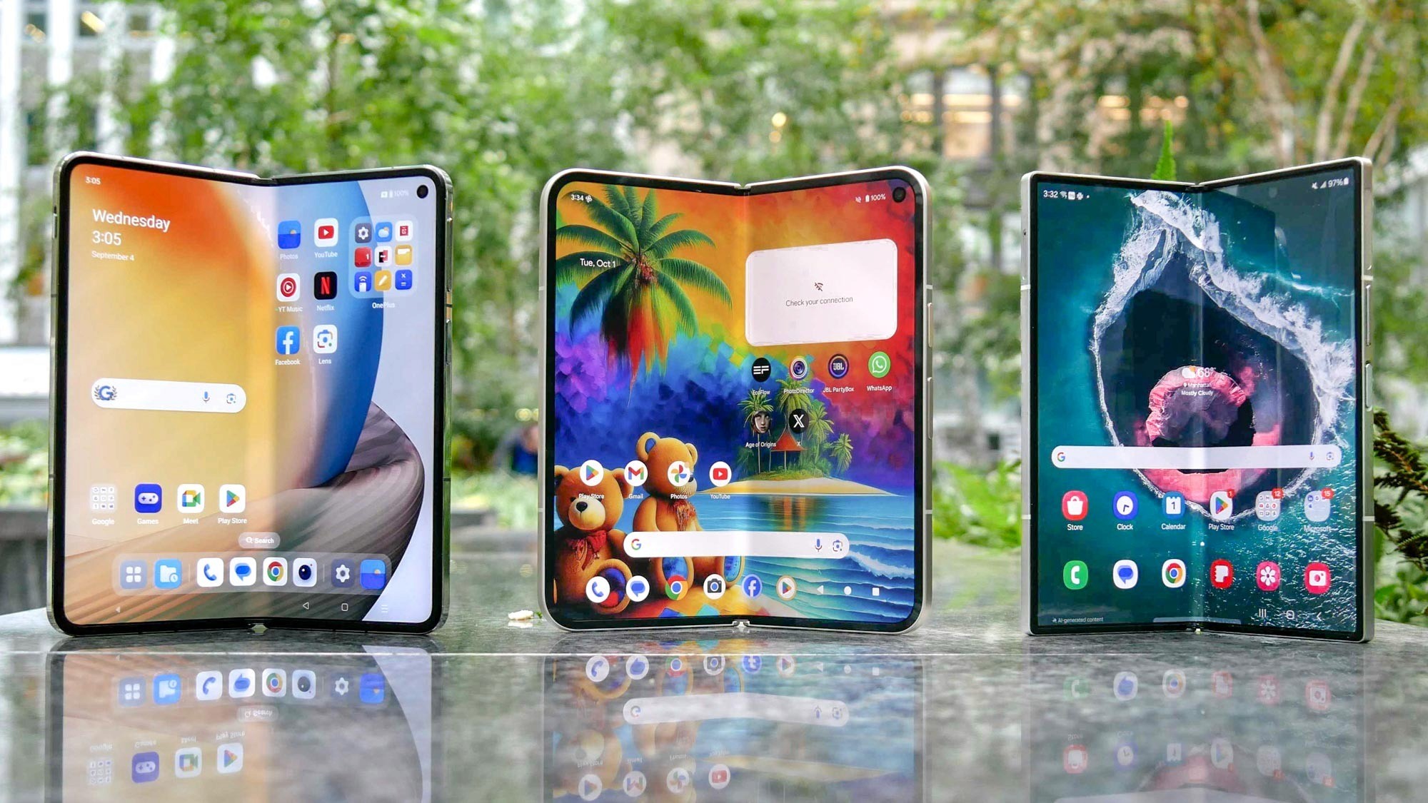 Three foldable smartphones with open screens displaying colorful app interfaces on a reflective outdoor surface.