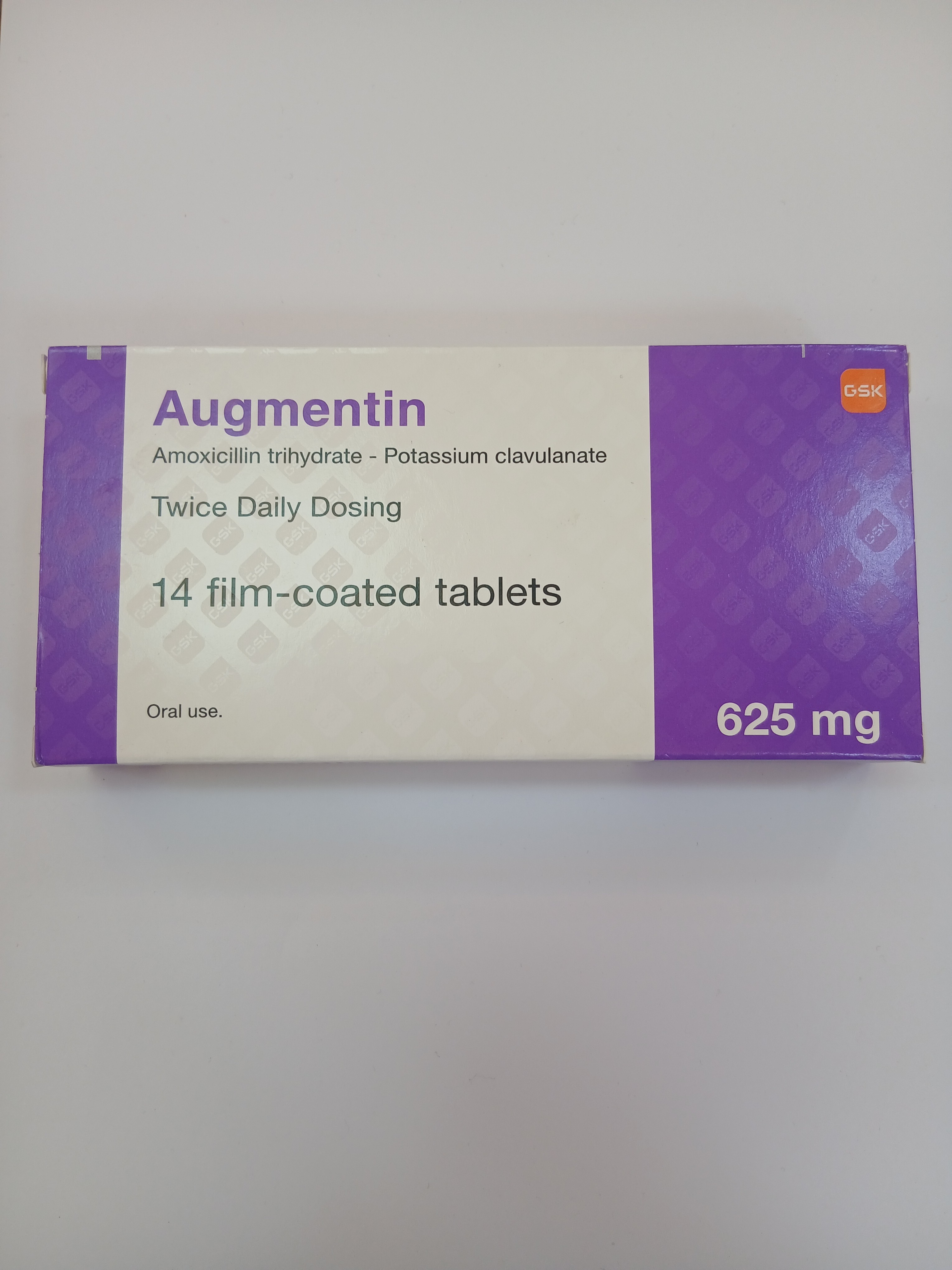 A white and purple cardboard box of Augmentin, containing 14 film-coated tablets of Amoxicillin trihydrate - Potassium clavulanate, with a dosage of 625 mg, is displayed on a light gray surface.