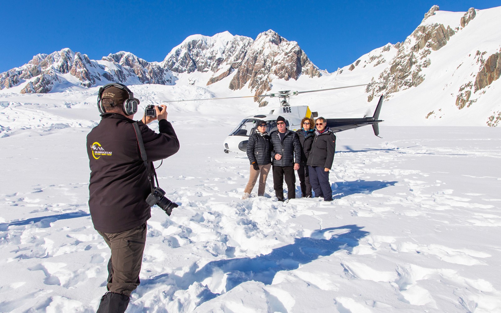 Grupo posando para una foto en el Glaciar Franz Josef con un helicóptero de fondo.