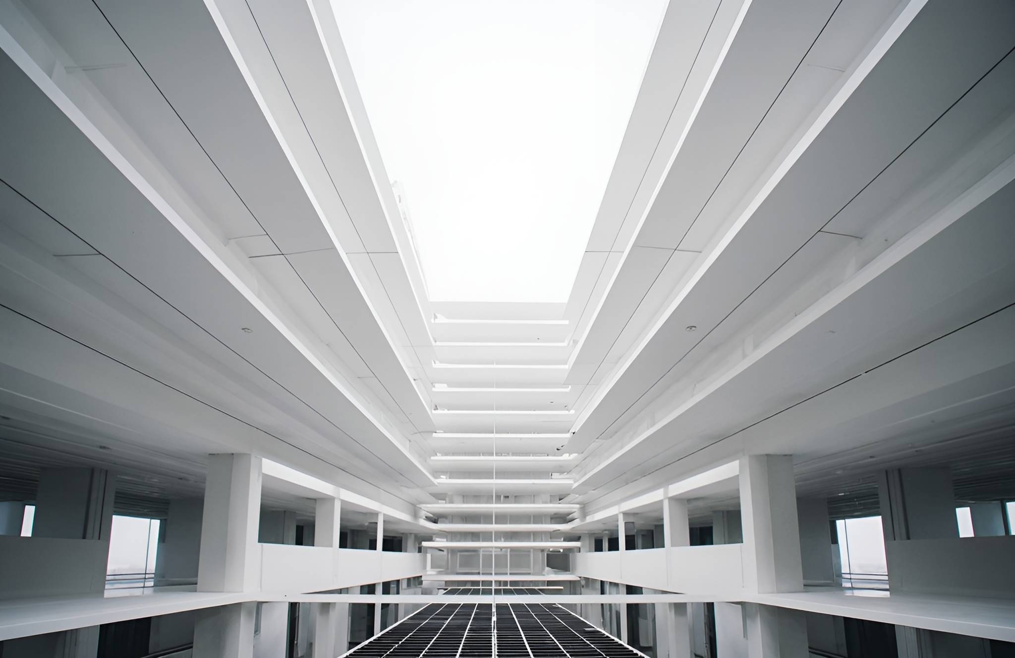 Minimalist building interior with white walls and multiple floors, viewed from below. Linear symmetry creates an airy, futuristic ambiance.