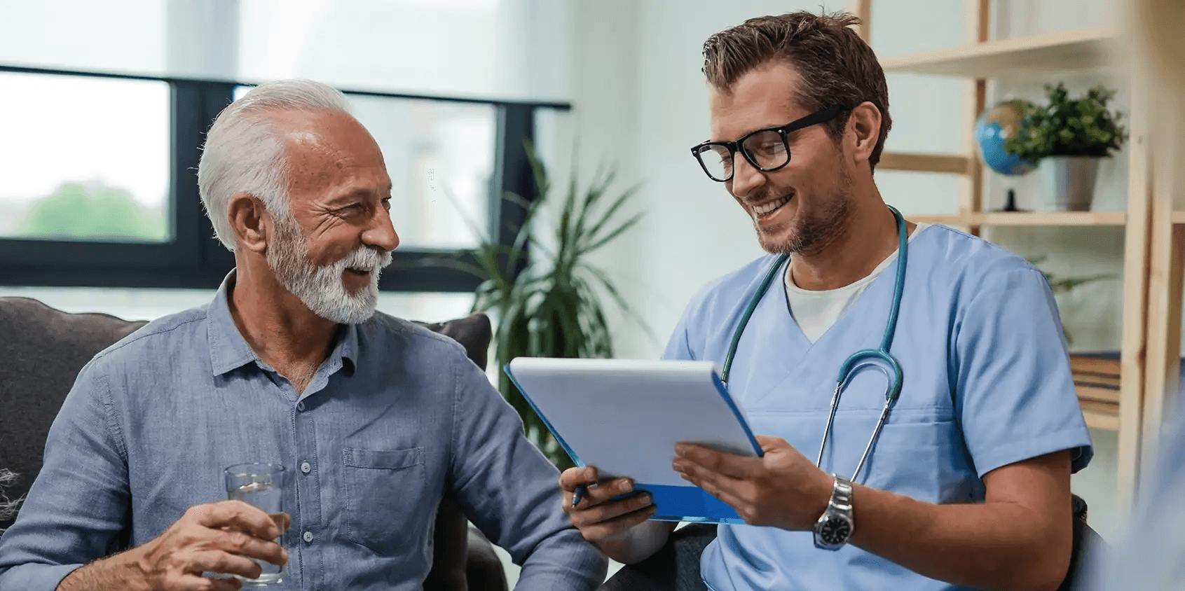 Healthcare professional and elderly man smiling while discussing information on a clipboard