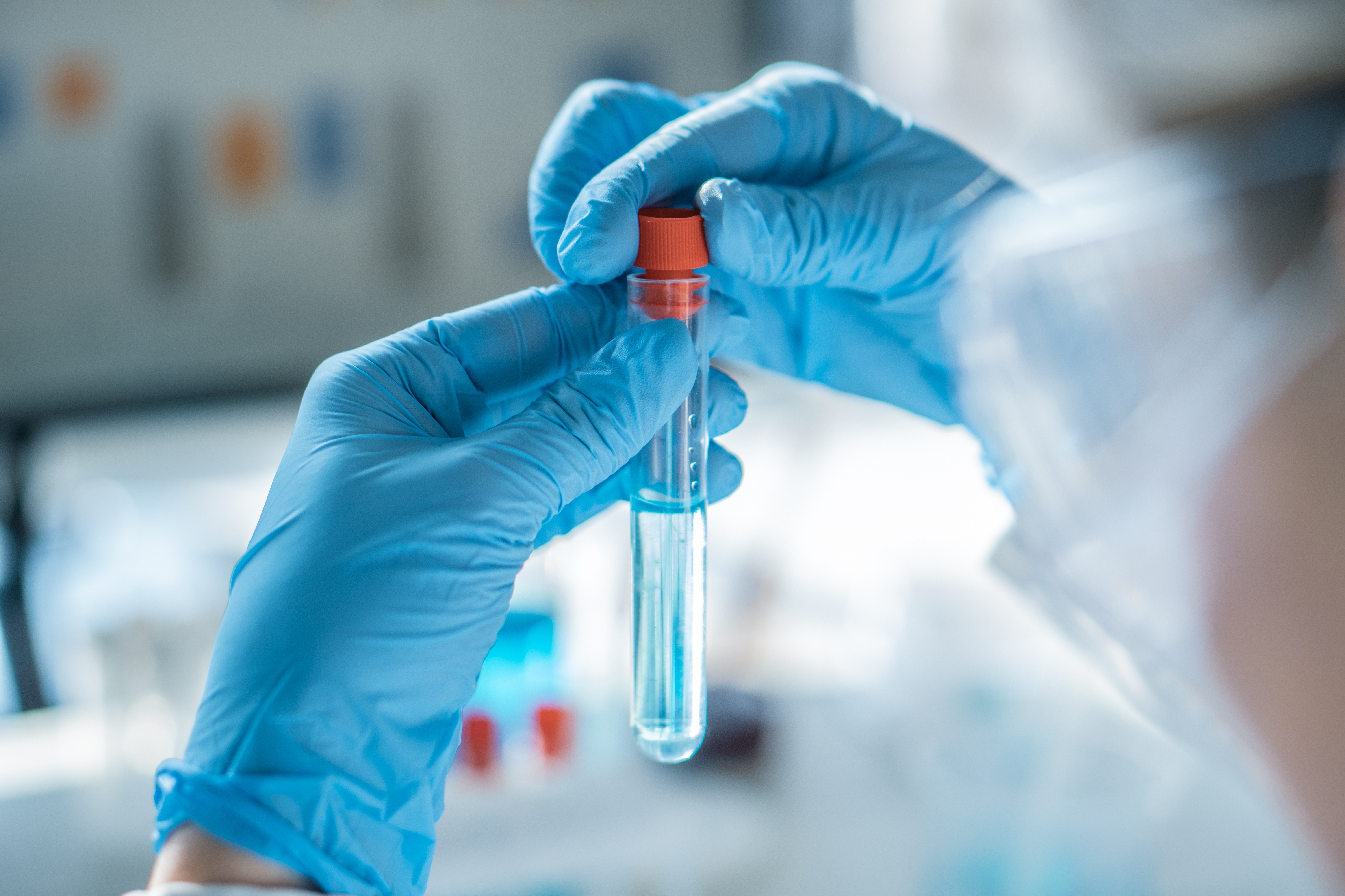 Two hands wearing gloves fixing a seal on a laboratory tube with clear liquid in it.