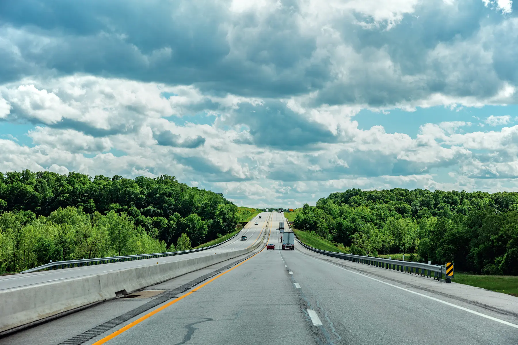 Open highway surrounded by green trees under a partly cloudy sky, representing GIA Group, LLC’s commitment to guiding truckers with clear answers and reliable insurance support.