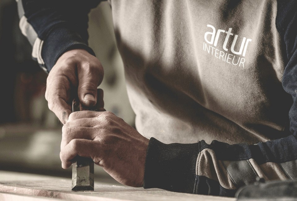 image of a craftsman working on a piece of wood wearing a sweater with a artur interieur logo