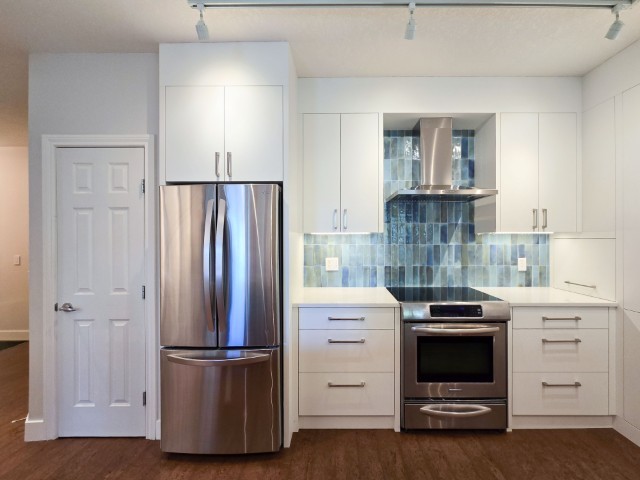Image of Modern kitchen with stainless steel appliances, white cabinets, and blue tile backsplash by KHD Homes.