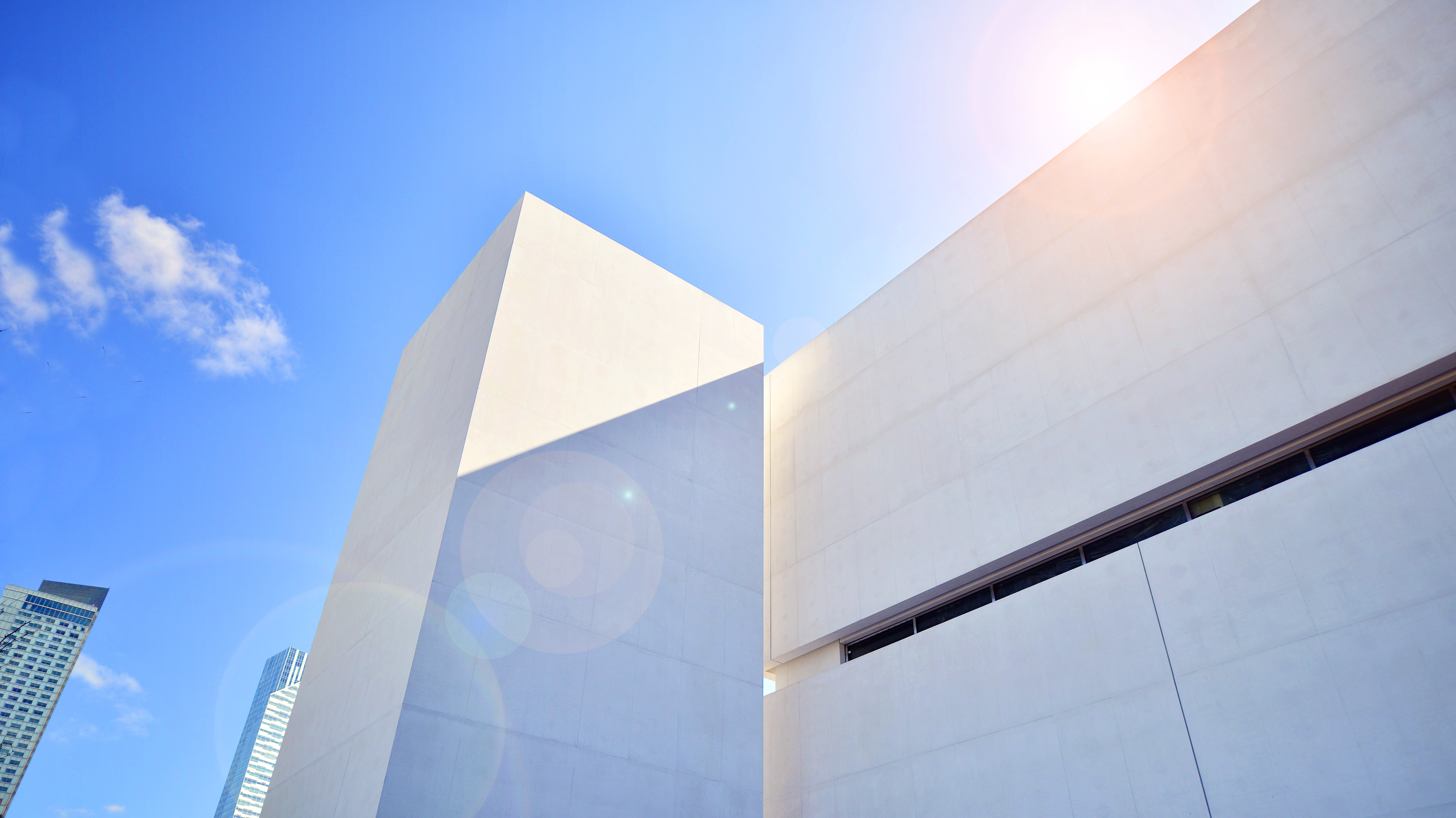 Modern white building with a clear blue sky and sun flare.