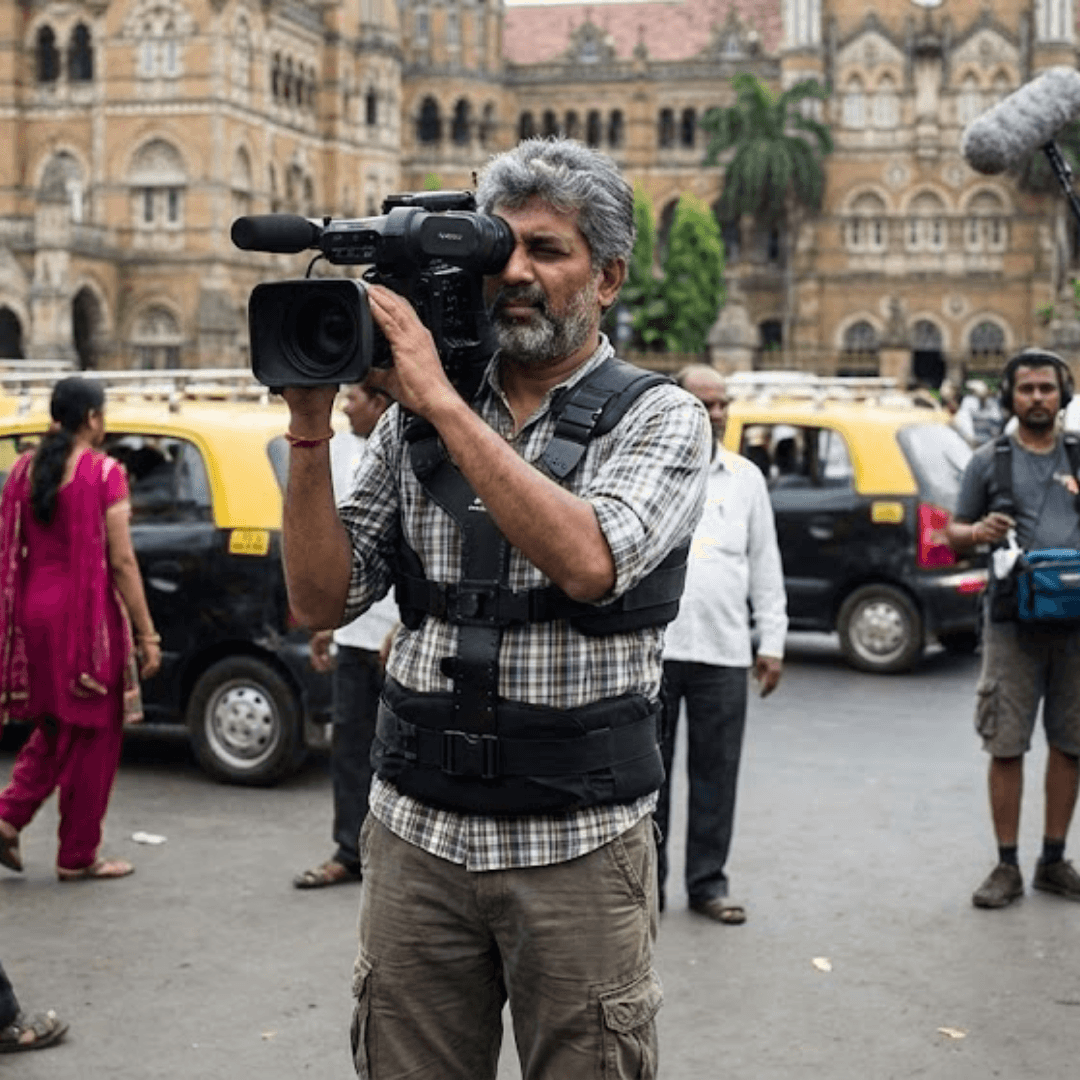 Documentary cameraman filming on a busy street using a shoulder-mounted camera rig.