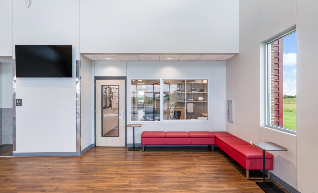Quiet lounge with red bench seating and a wall-mounted TV at Greenville Fire Department Administration & Training Facility, by Martinez Architects