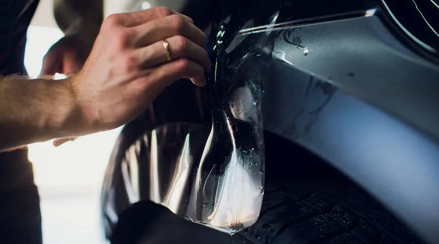 Applying protective film to car bumper.