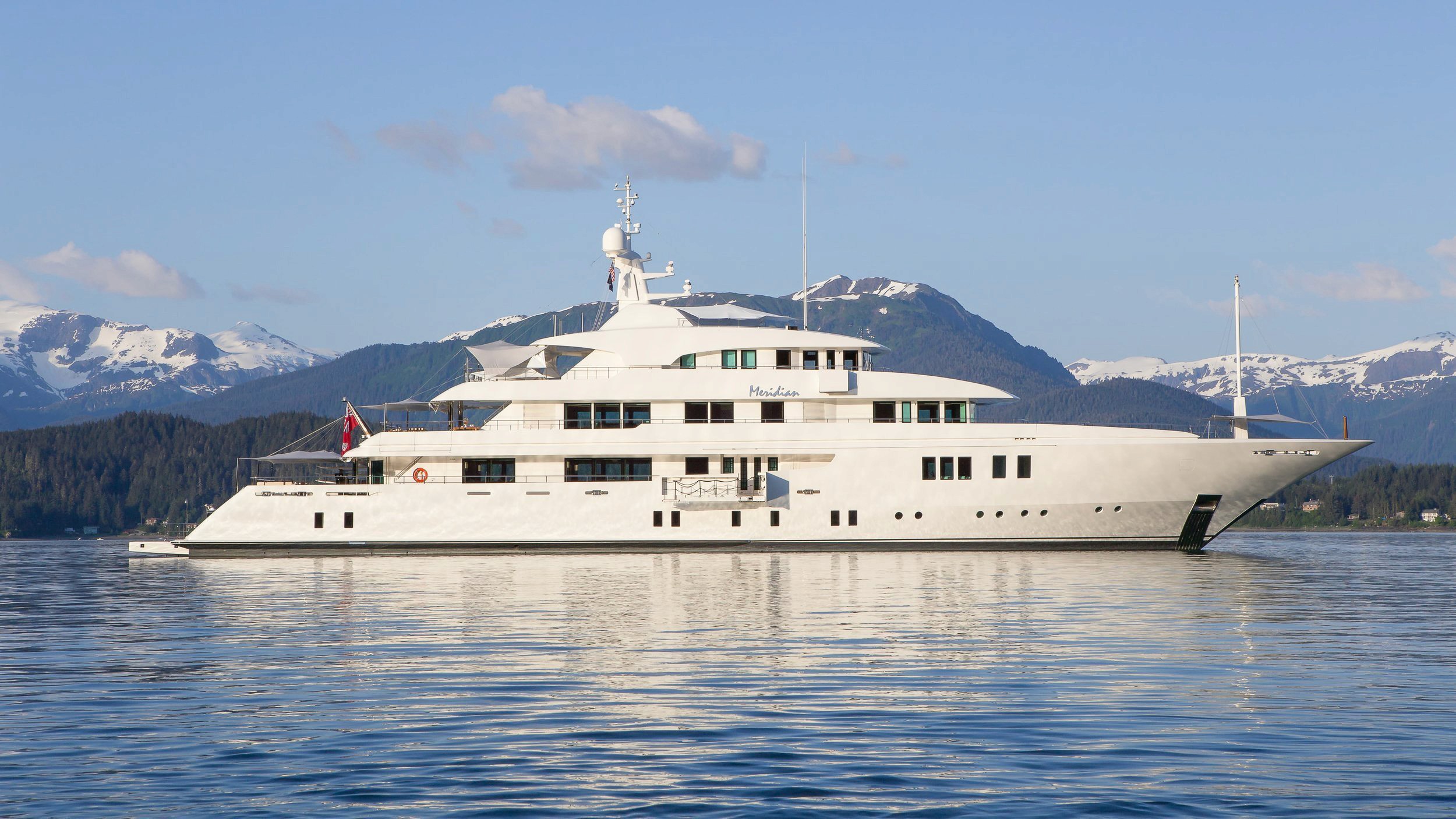 White superyacht named "Meridian" in calm water with snowy mountains.