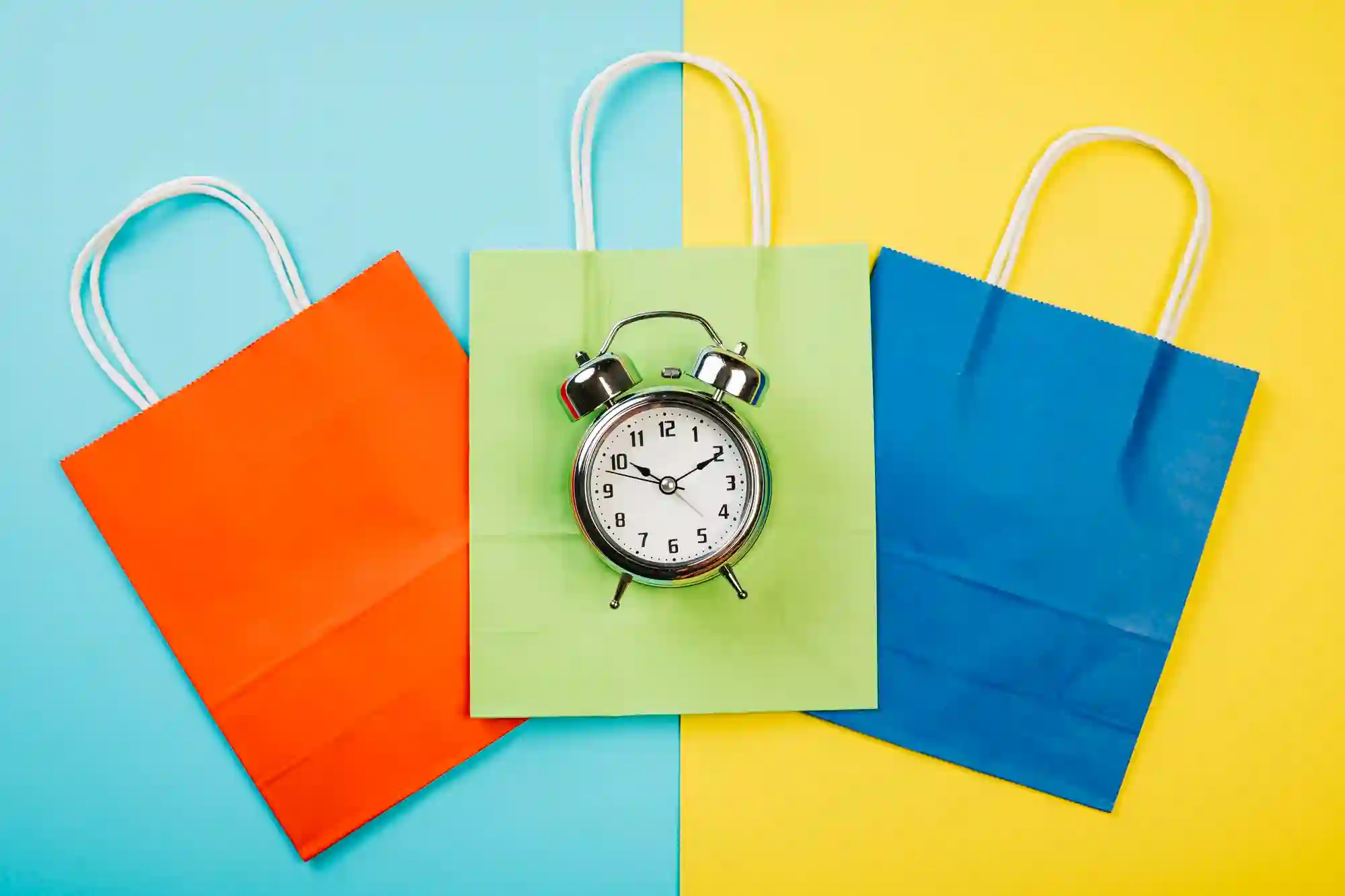 Three colored shopping bags with an alarm clock on the middle one.