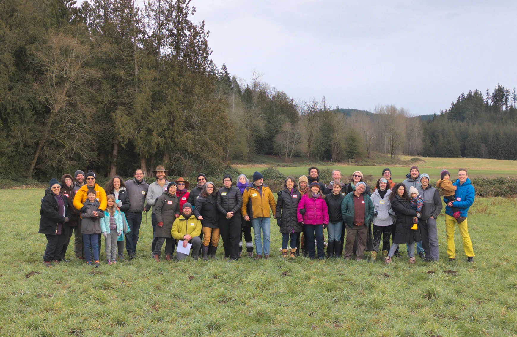 A large group of community members standing together outdoors on open land at Rooted Northwest.