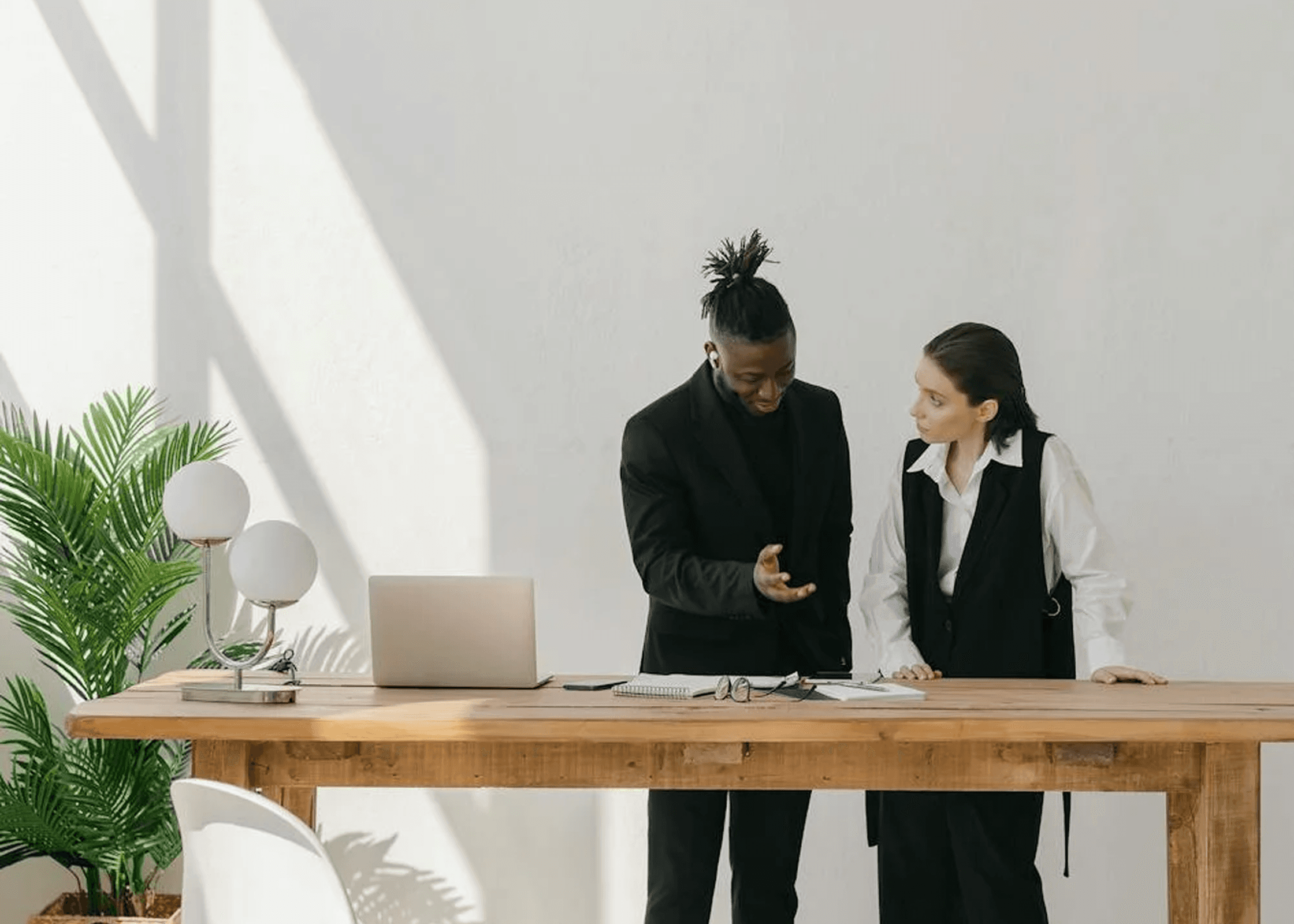 Two colleagues discussing work at a minimalist wooden desk.