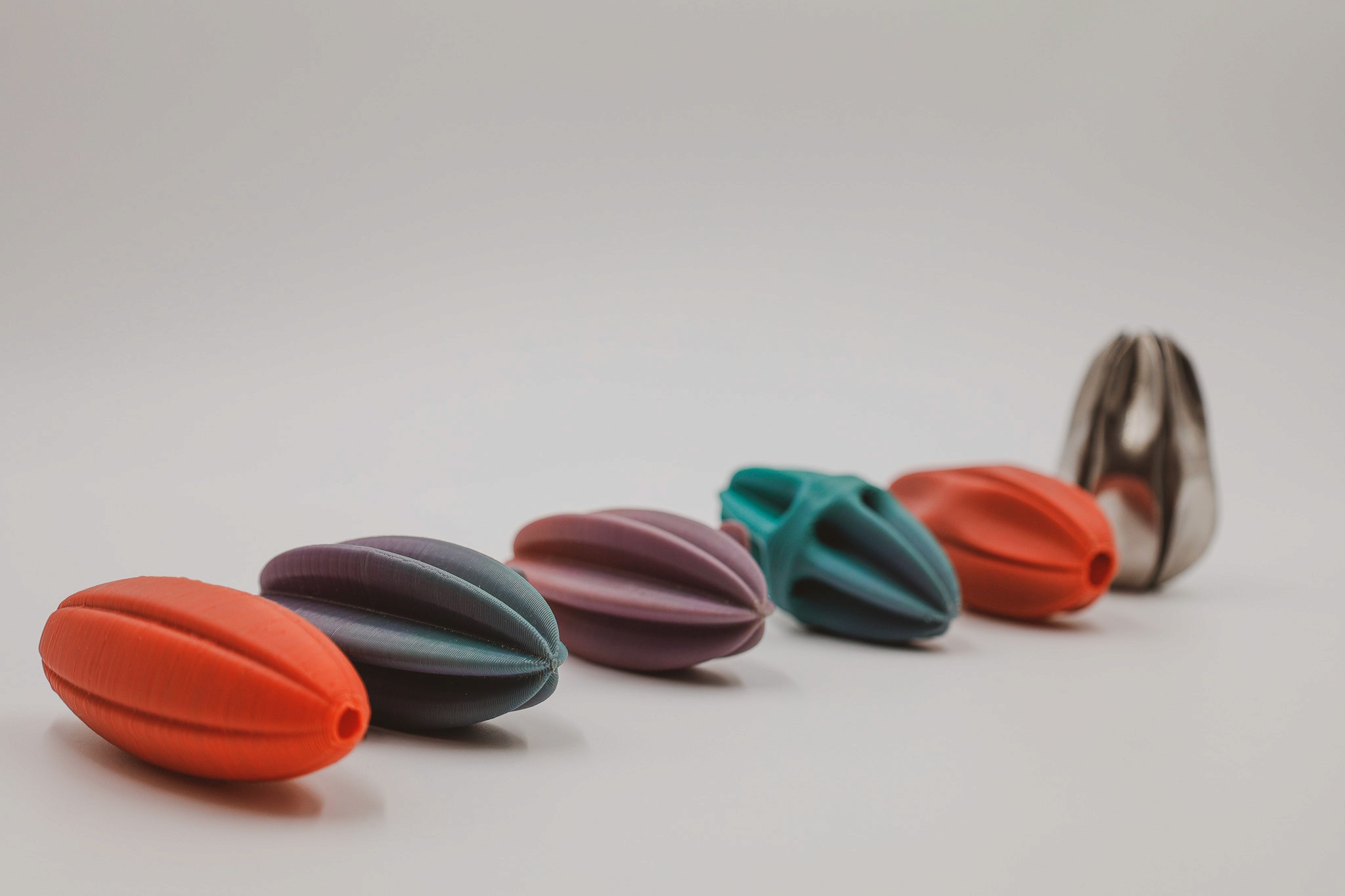 A line of colorful,PLA printed squeezers progressively opening to reveal a metallic one at the end, all against a neutral background.