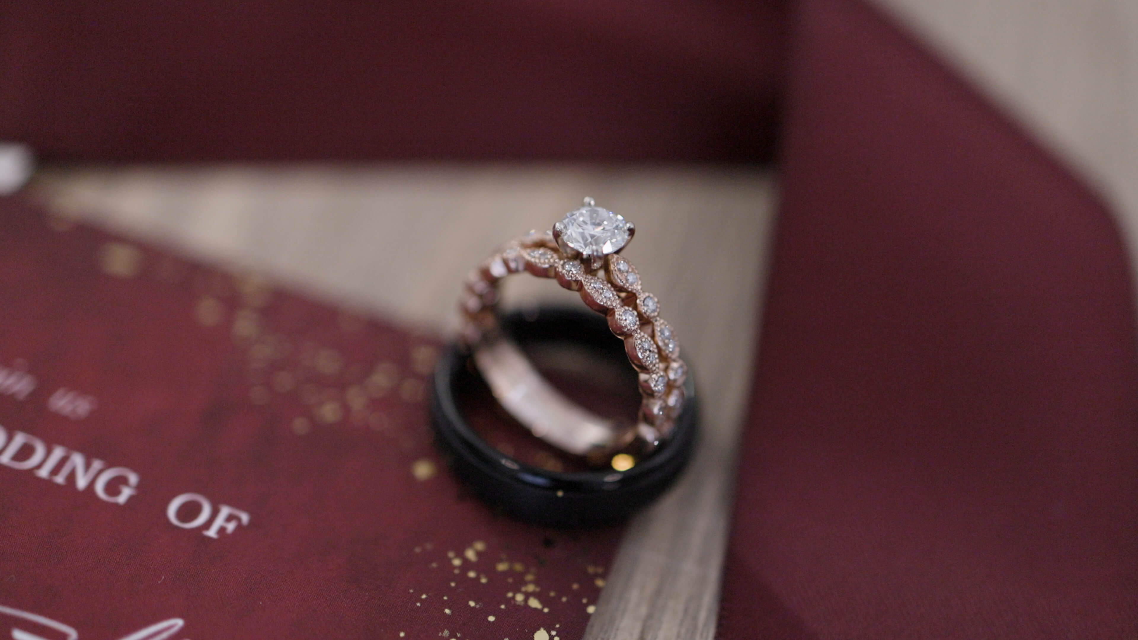 Two wedding rings balancing on each other with maroon red decorations in the background