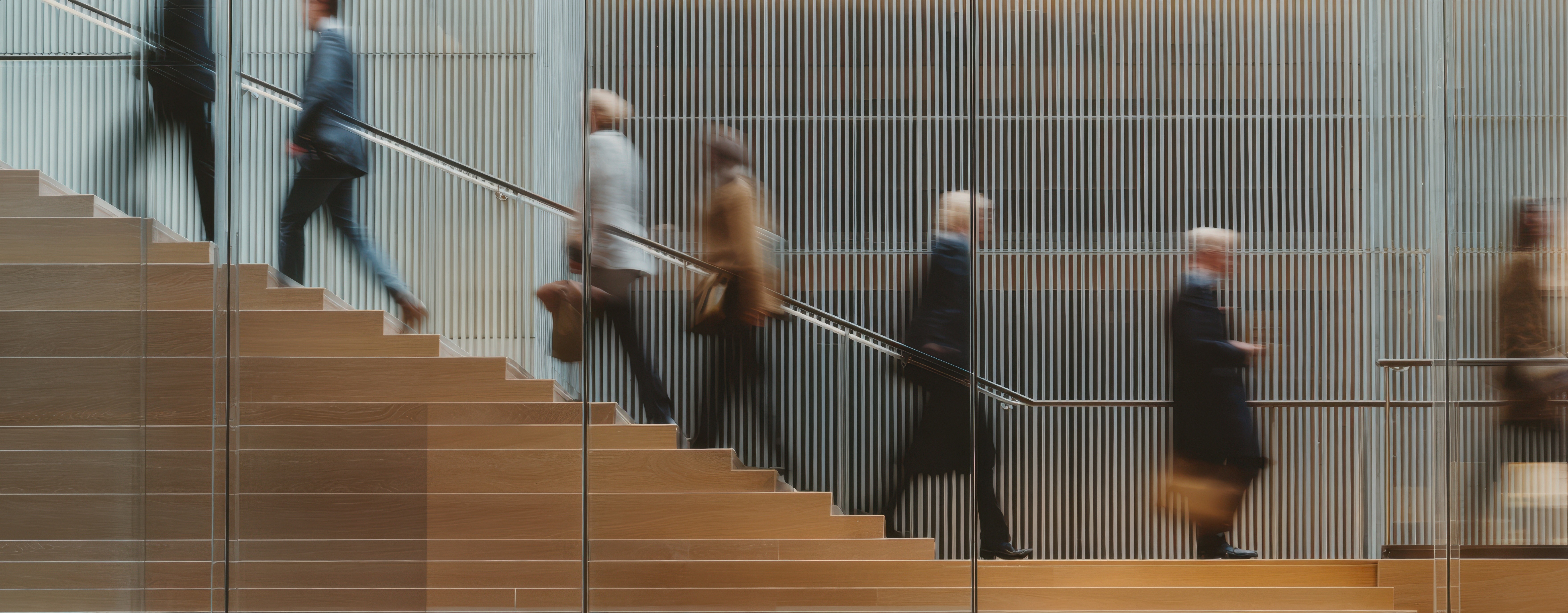 Blurred professionals moving up a staircase in a modern office, symbolizing organisational change, momentum, and continuous improvement.