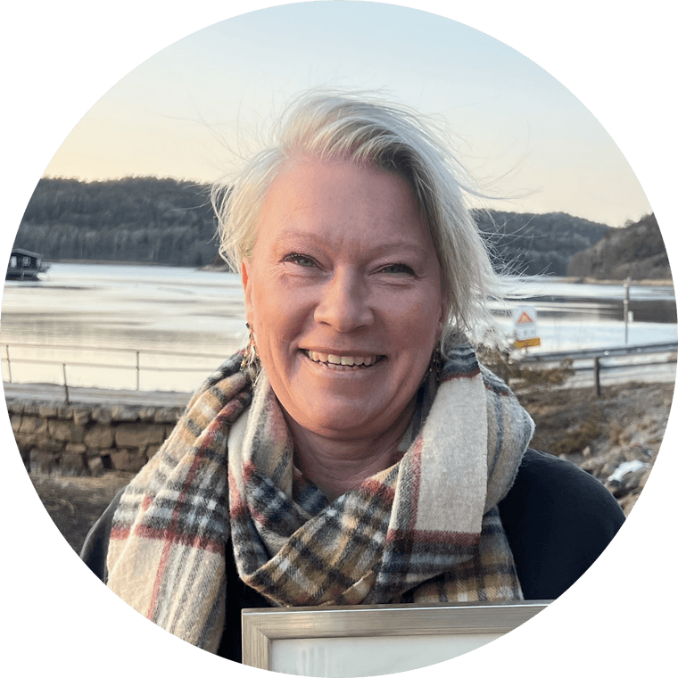 A young person with curly hair smiles at the camera while sitting in front of a laptop against a dark background.